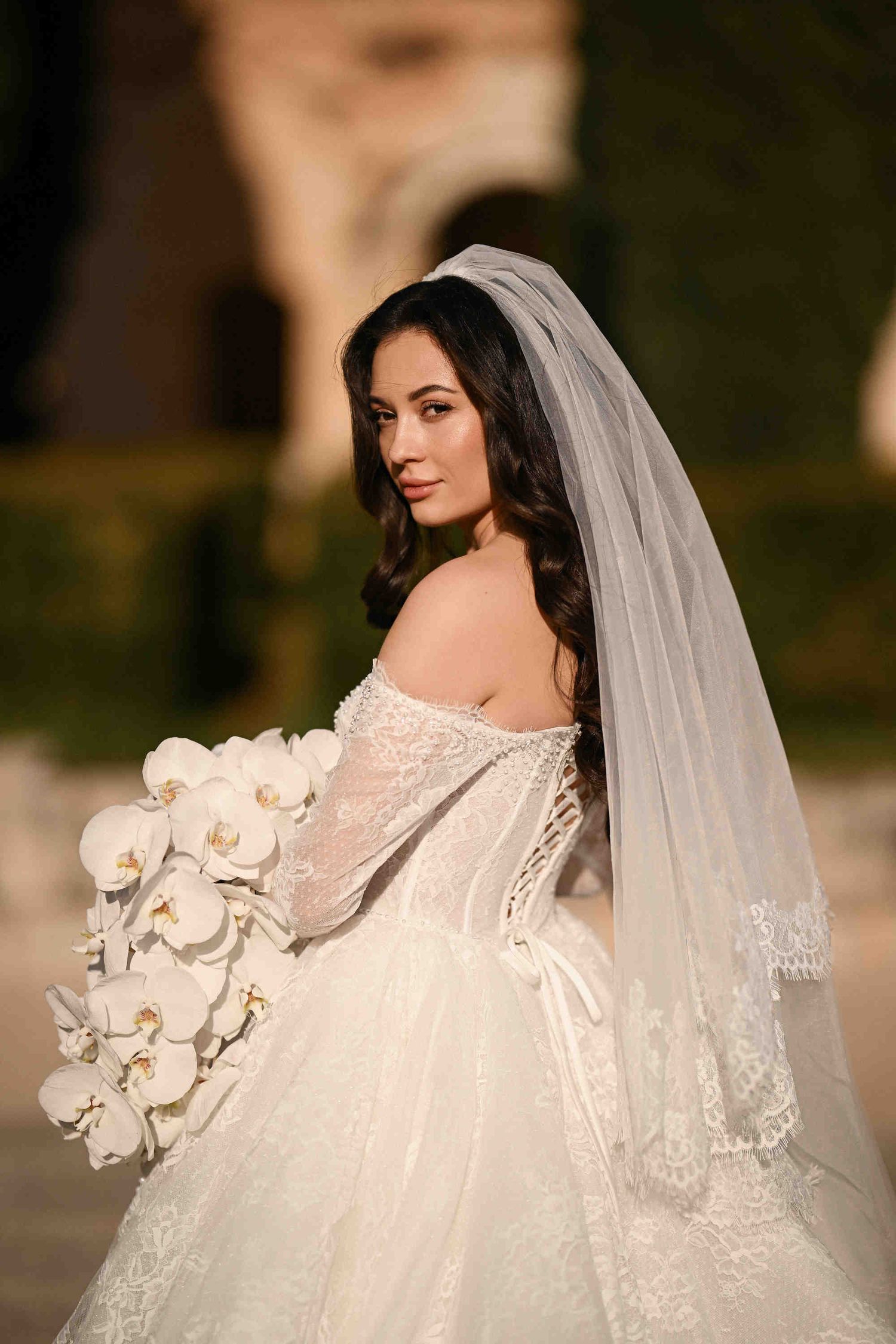 Intimate bridal portrait with an orchid bouquet, looking into the lens at the Monasterio de Santa María de la Valldigna in Spain.