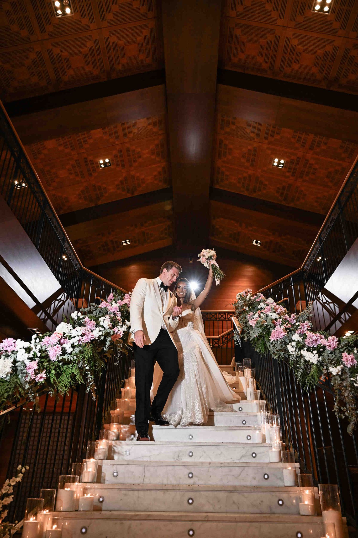 Bride and groom walking down a decorated marble staircase with candles during their wedding entrance.