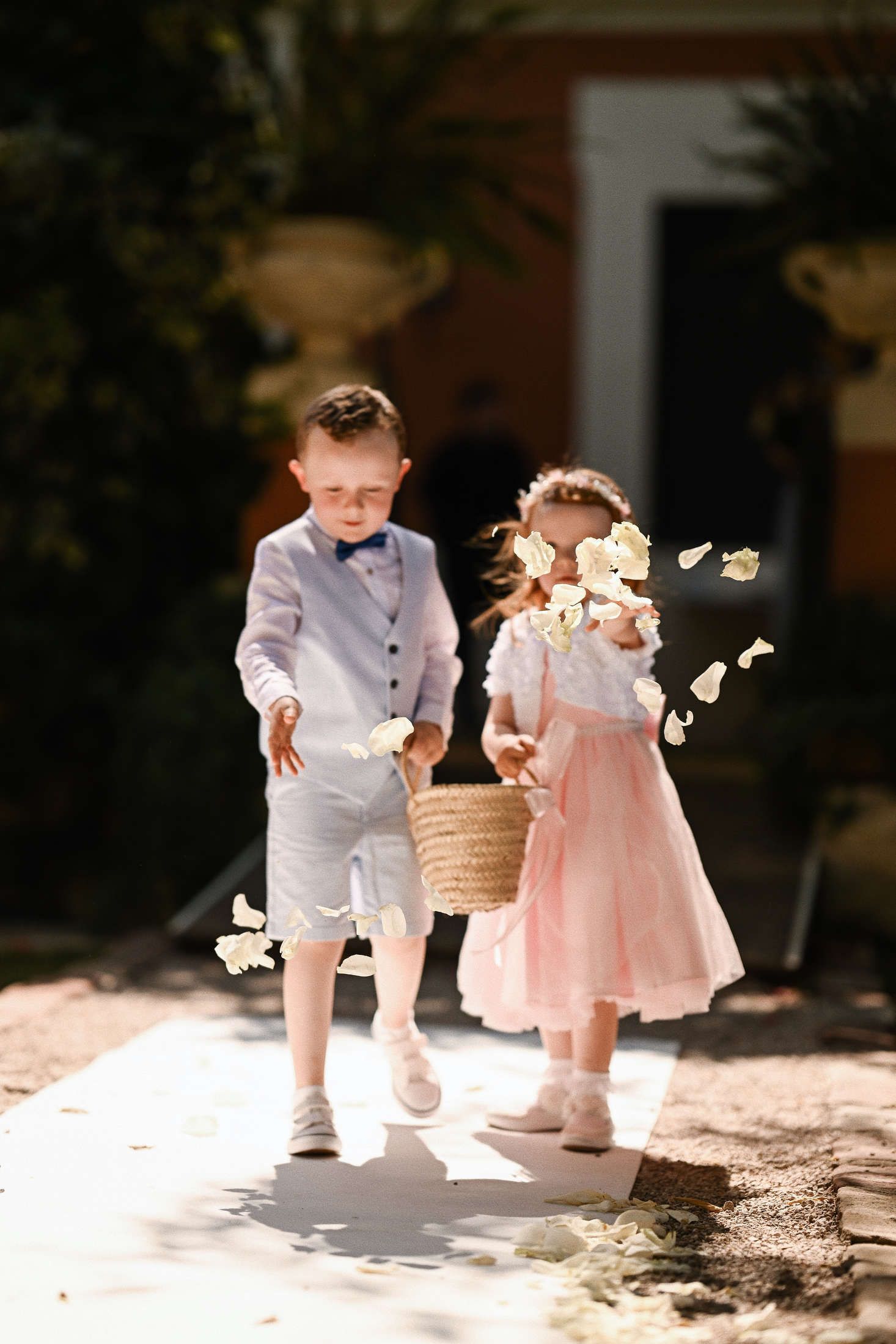 Cute flower girl and page boy throwing pink rose petals down the aisle during an outdoor wedding ceremony at Villa Dela.
