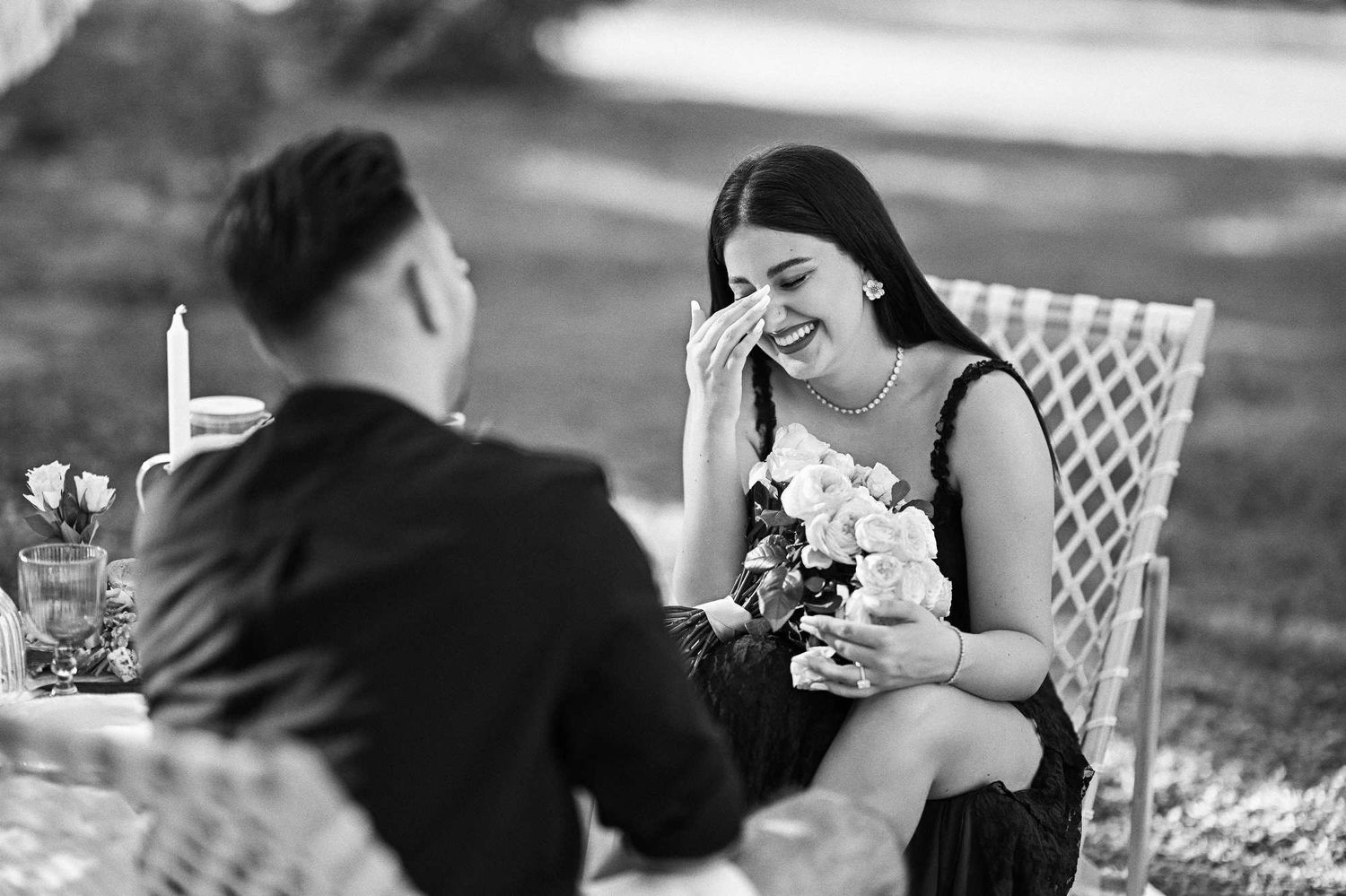 Black and white shot of a newly engaged woman wiping happy tears while holding roses after a Viveros Park proposal.