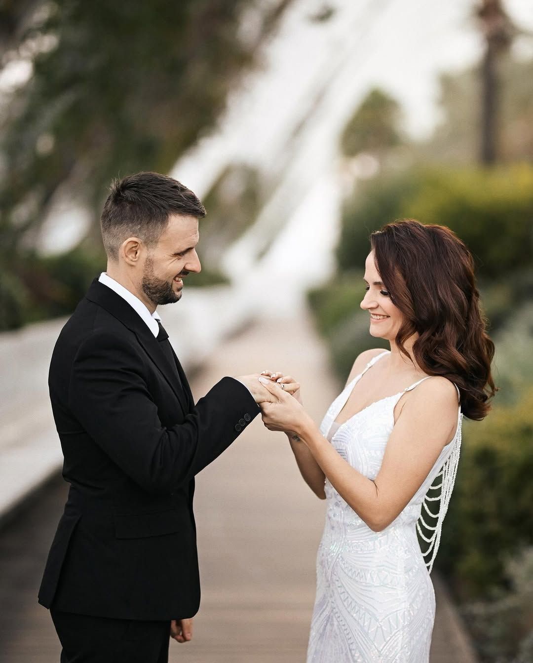 A groom in a black suit places a wedding ring on his smiling bride's finger during an intimate ceremony in Valencia.