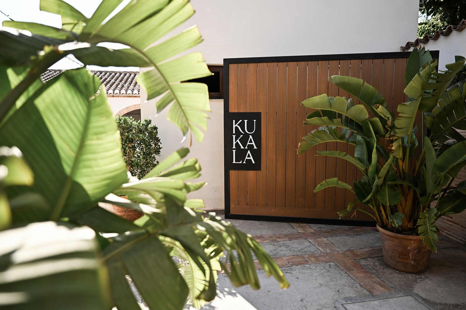 Editorial view of Alquería Kukala wooden gate sign framed by large tropical green leaves in Valencia Spain.