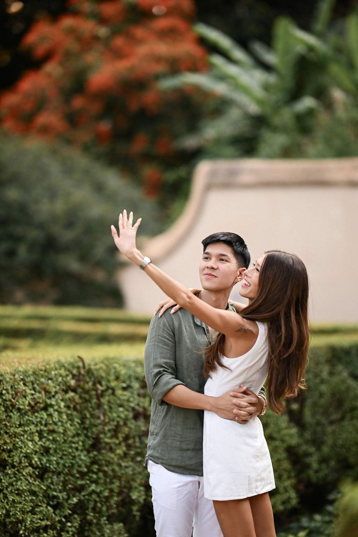 A man hugging his partner from behind beside manicured garden hedges shortly after he decided to propose in Valencia.