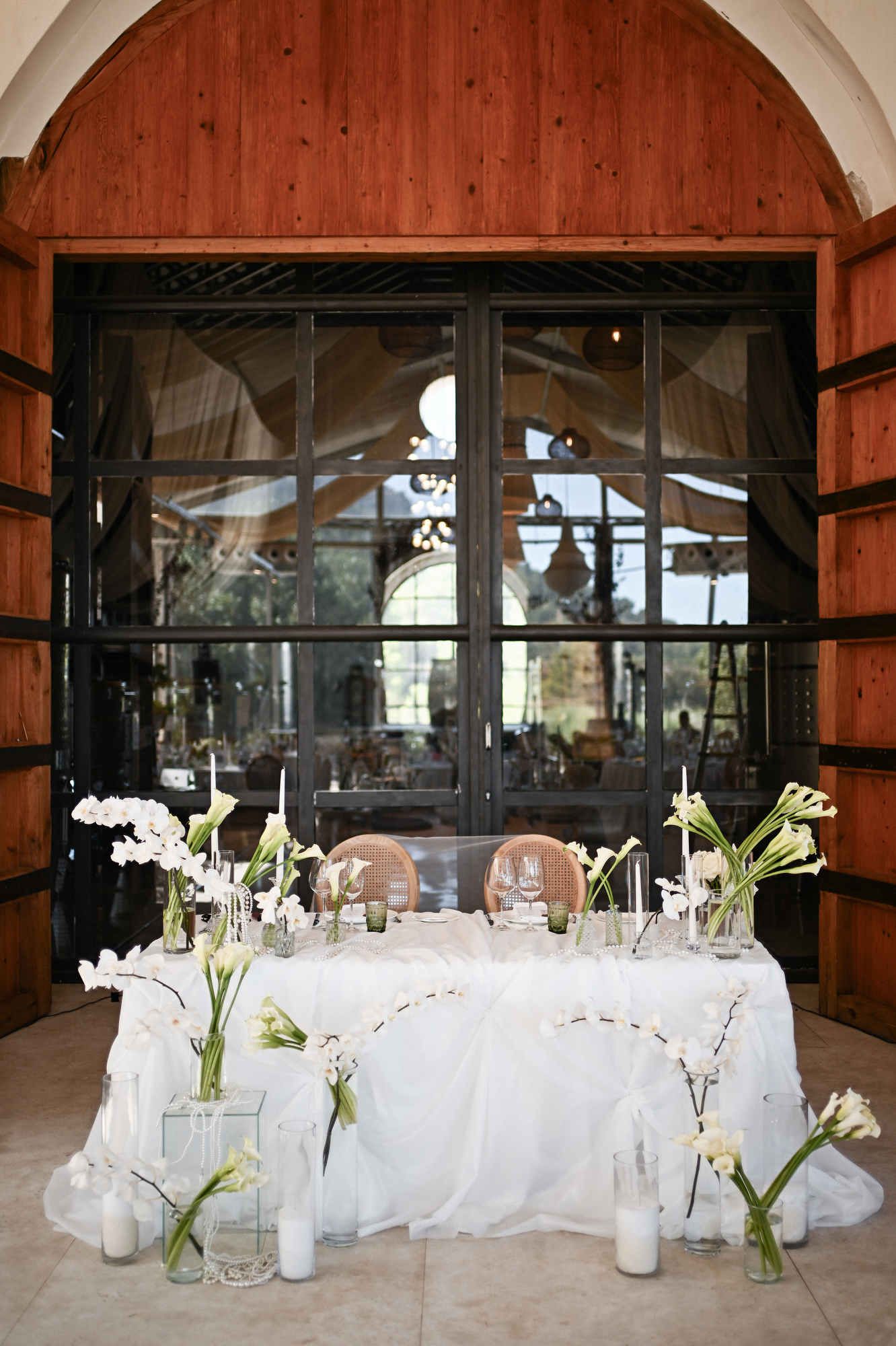 Elegantly styled wedding head table decorated with white orchids and candles in front of Bodega MASOS.