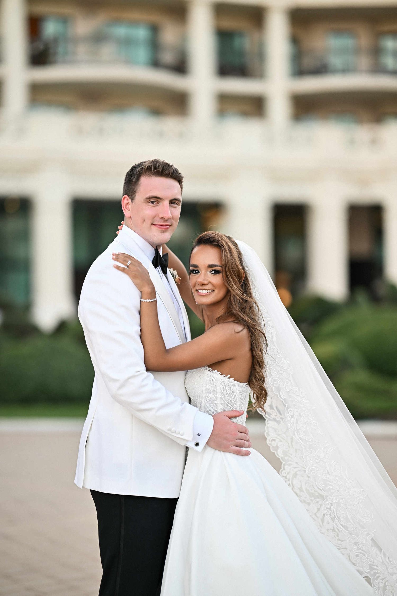 Newlyweds embracing in front of the classic colonnade facade at Hotel Las Arenas Balneario Resort Valencia