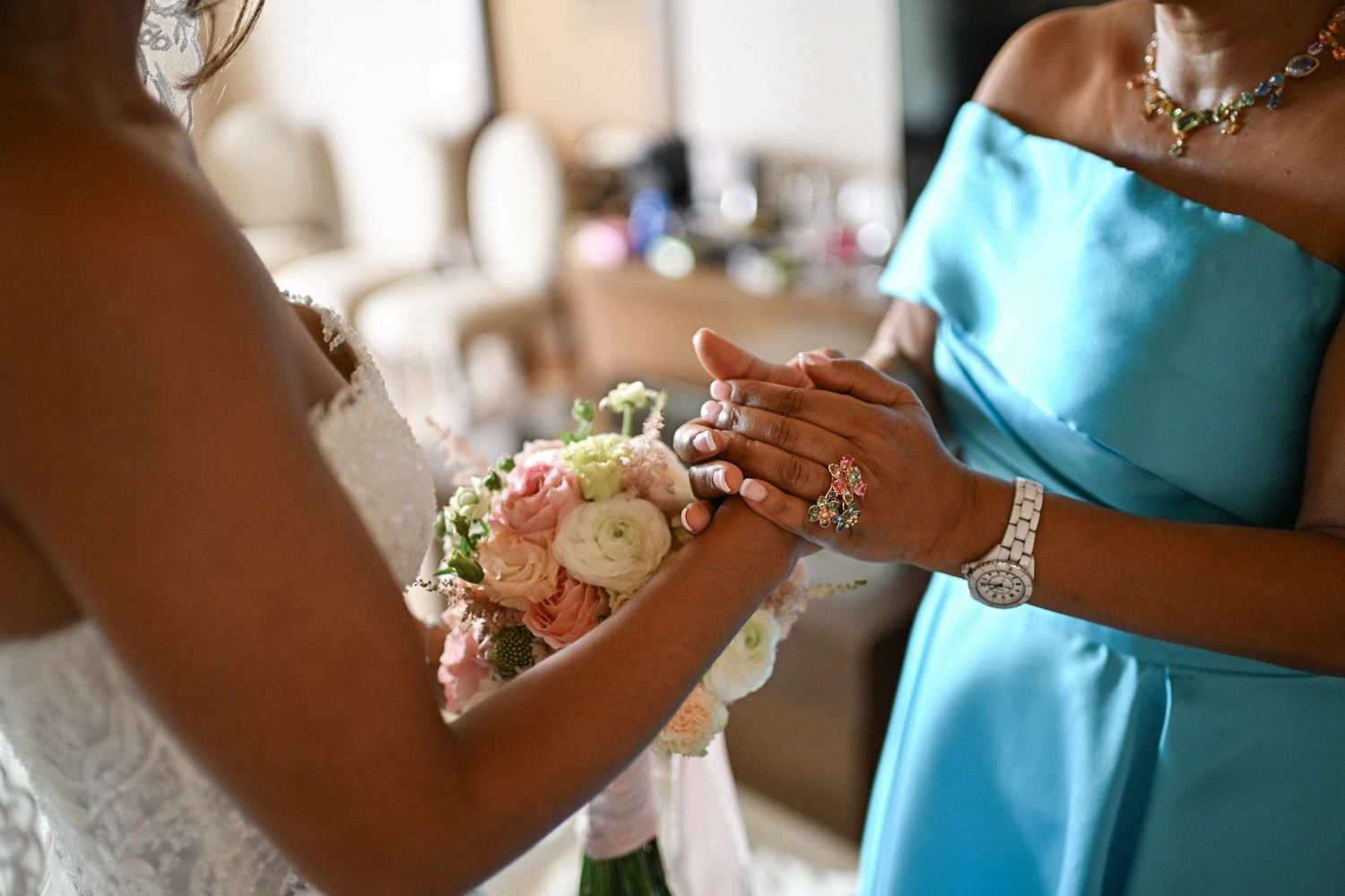Close-up of the mother of the bride in a blue dress tenderly holding her daughter's hands before the wedding