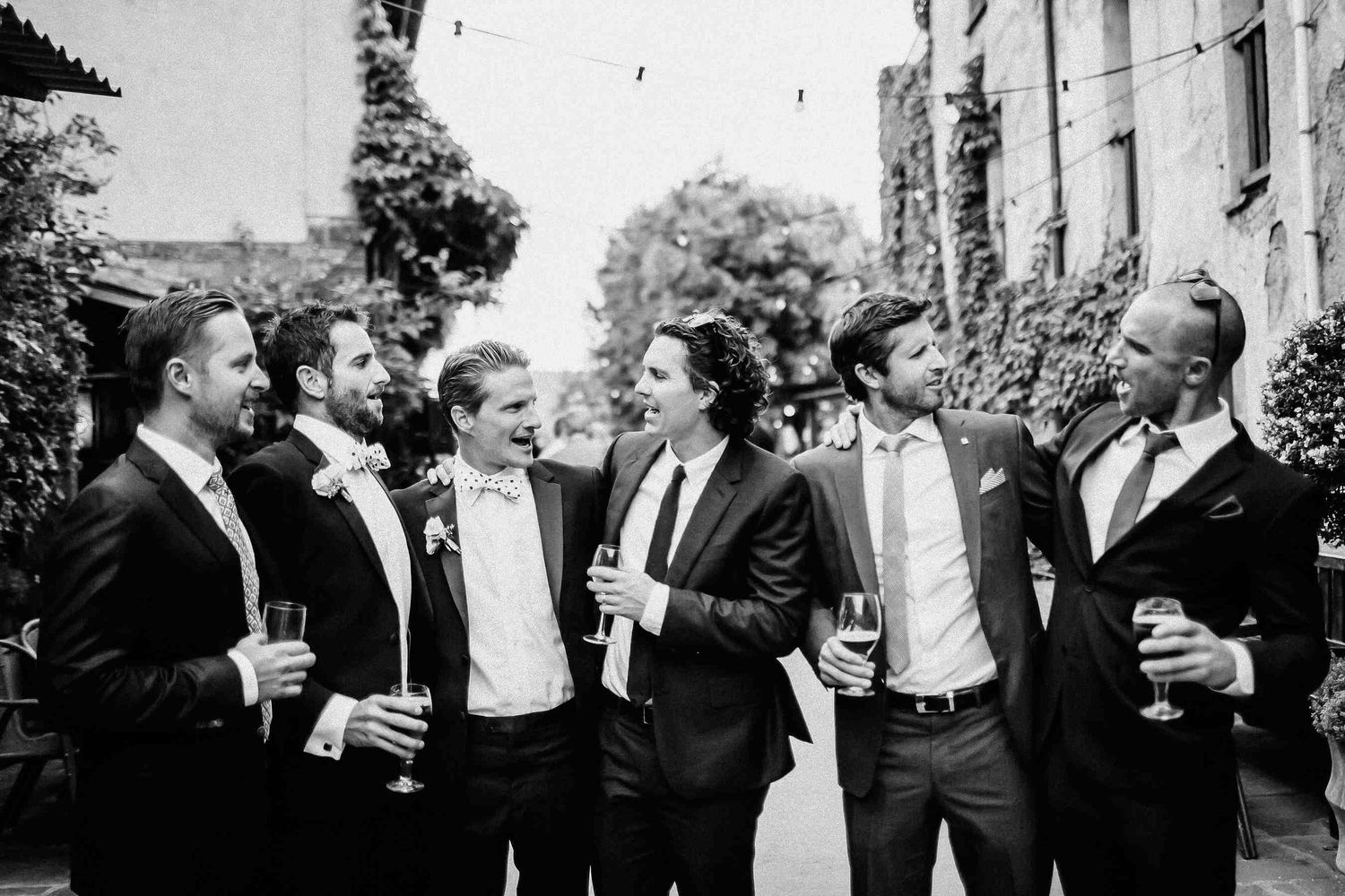 Groom's friends chatting in the historic streets of Spanish village. Authentic black and white reportage-style wedding photography - Darista