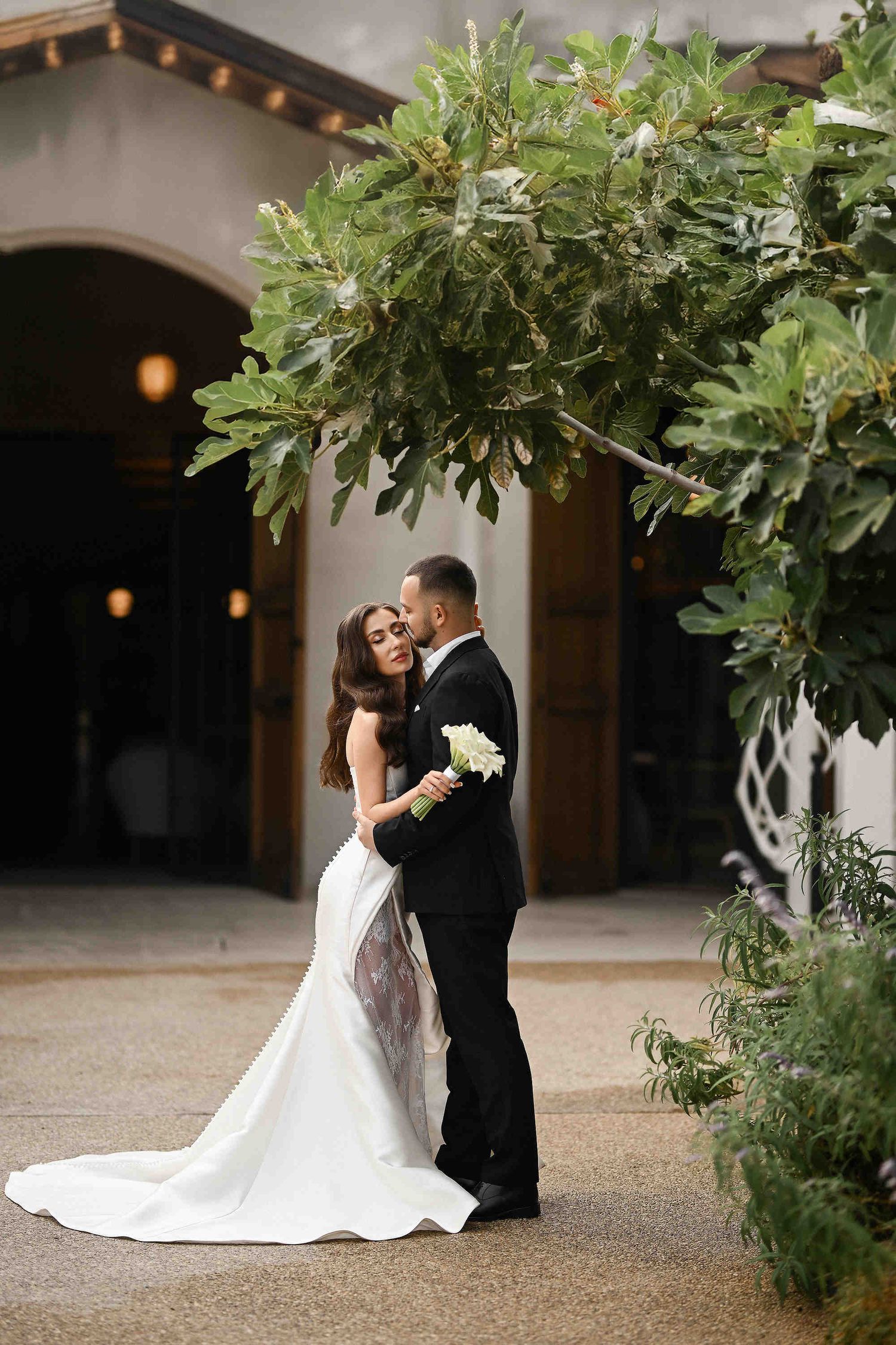 Groom embracing his bride with a stunning Mediterranean manor in the background, documented by a professional wedding photographer