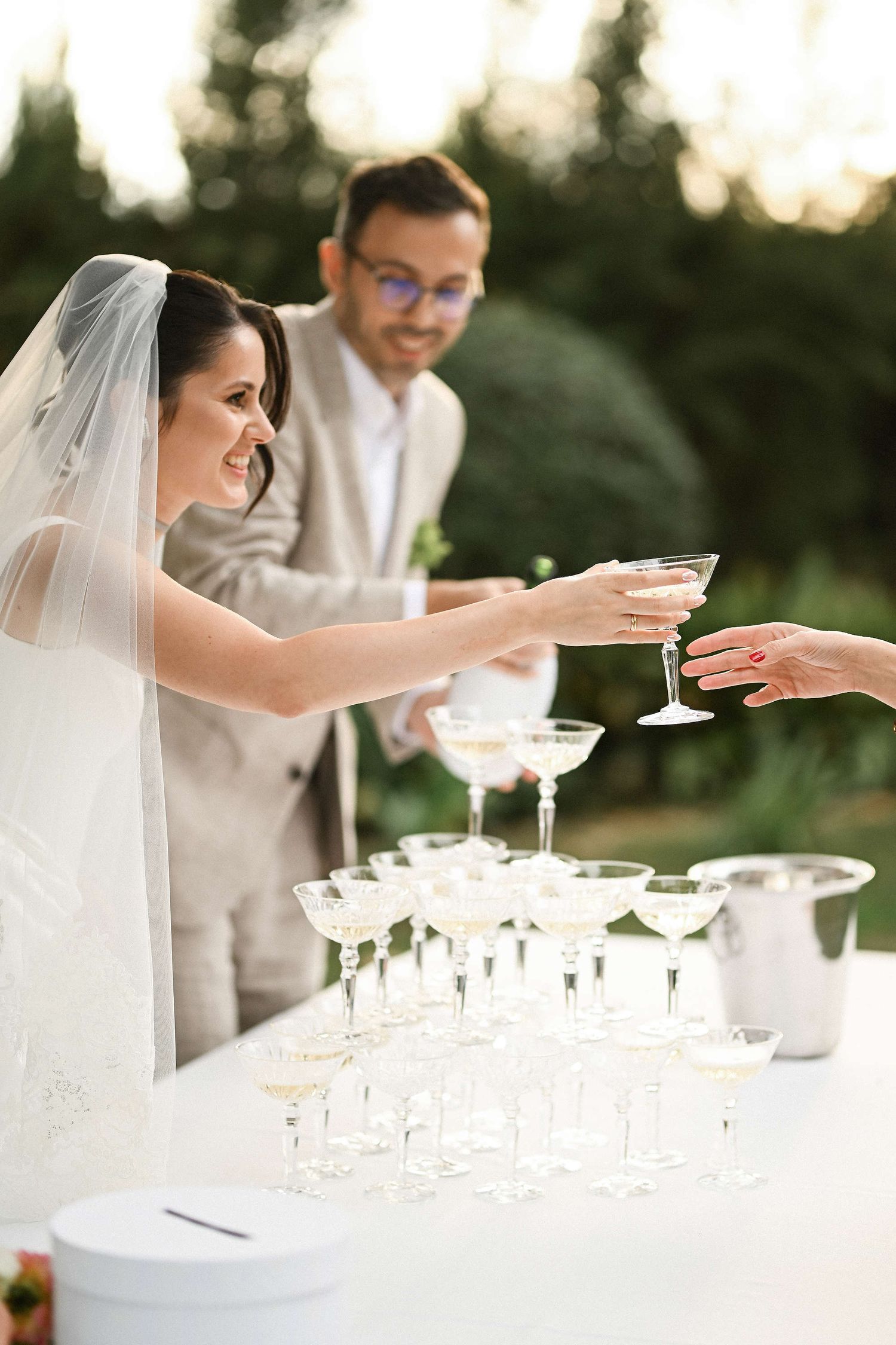 The bride and groom joyfully pouring champagne for guests, kicking off the relaxed cocktail hour celebration