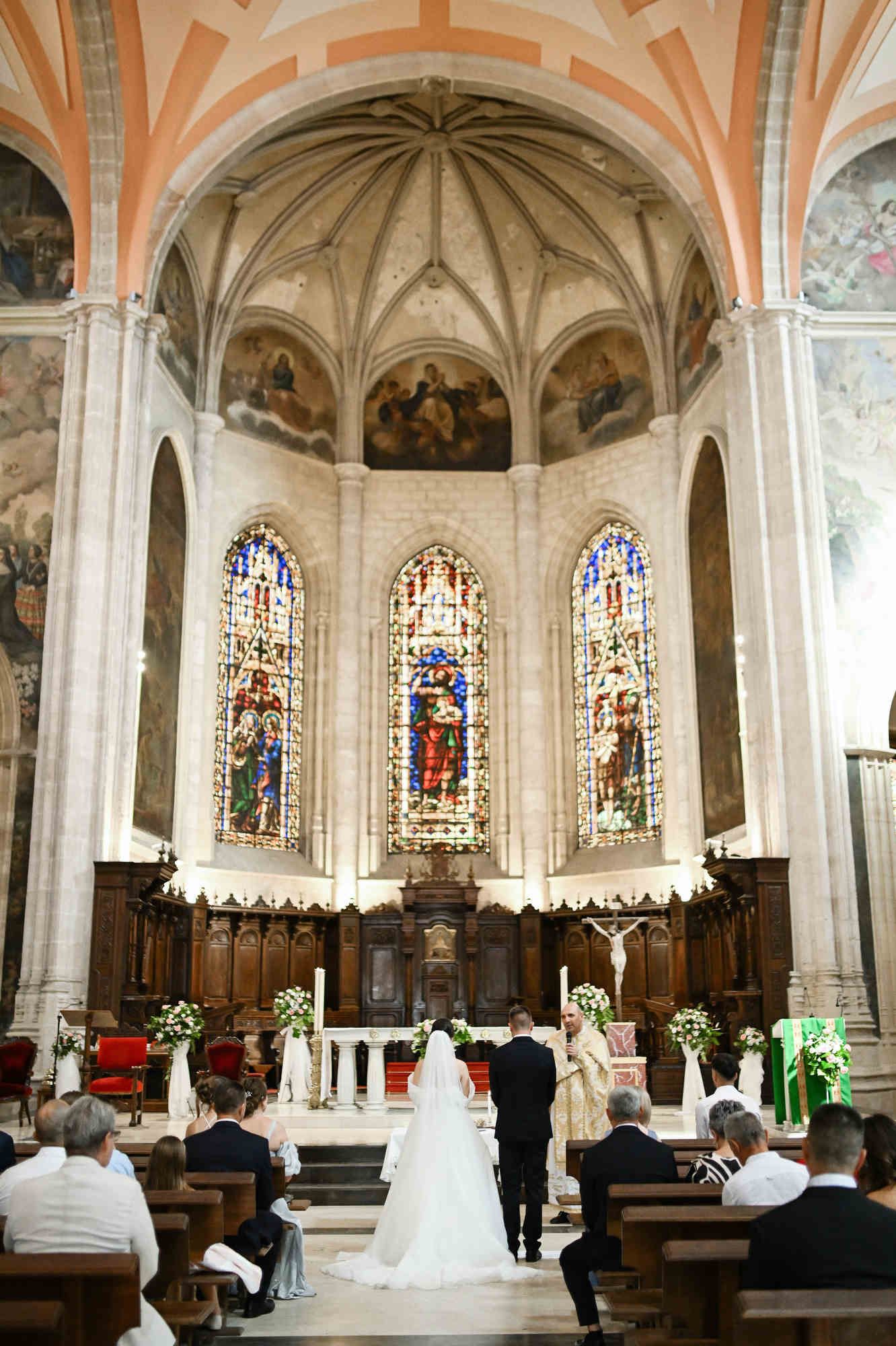 Wide shot of a Valencia church wedding showing the bride and groom at the altar under a grand dome with vintage stained glass windows.