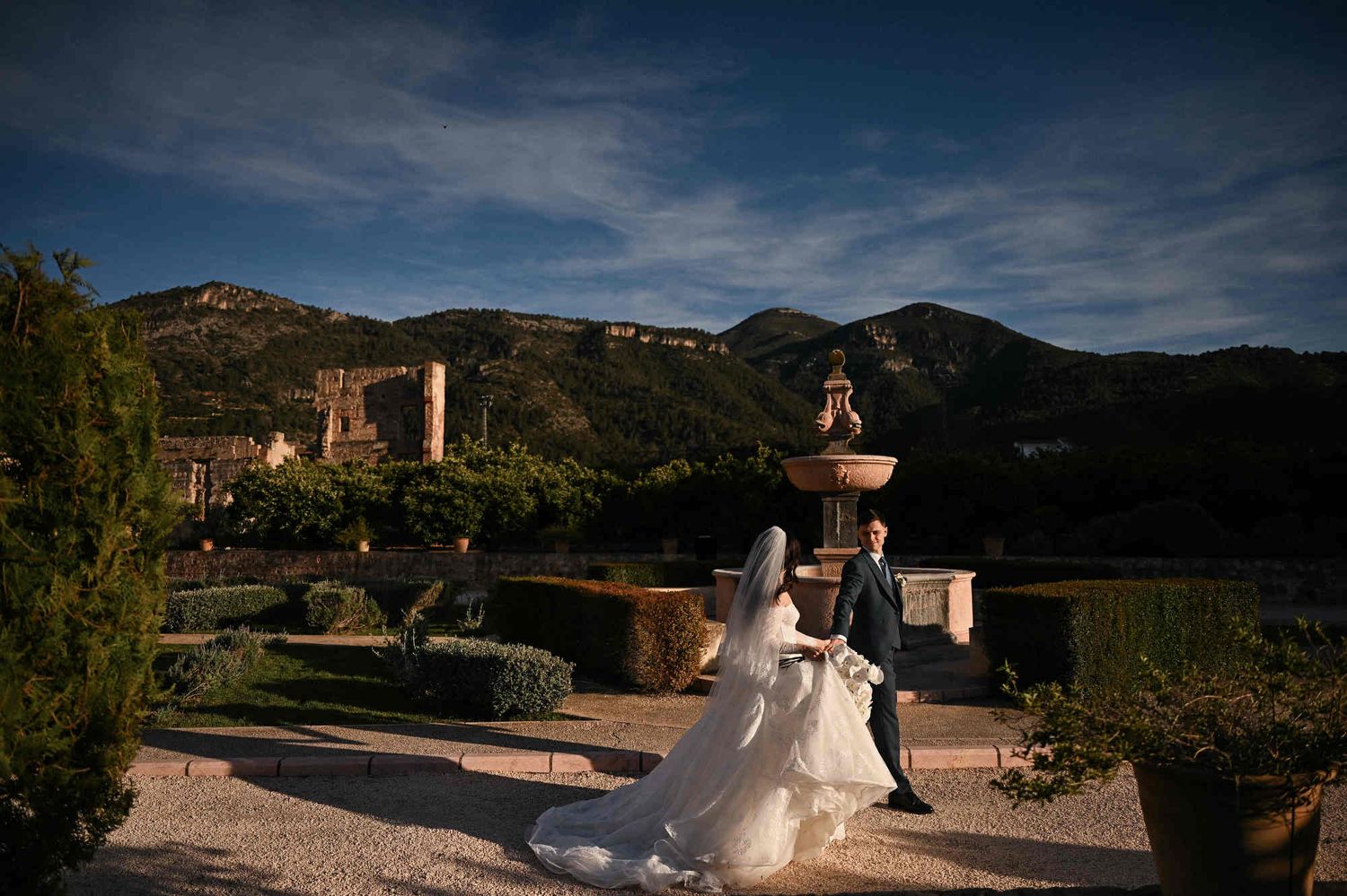 Newlyweds walking towards the exit of Monasterio de Santa María de la Valldigna with sunset mountains in the background, Valencia.