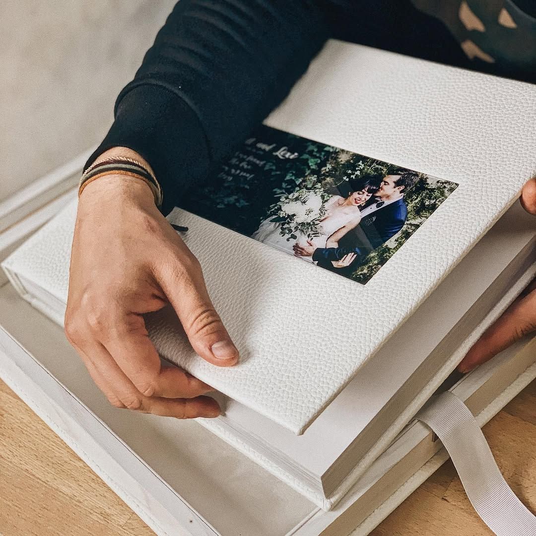 Hands holding a custom handmade wedding album inside a premium white leather storage box by a wedding photographer in Spain.