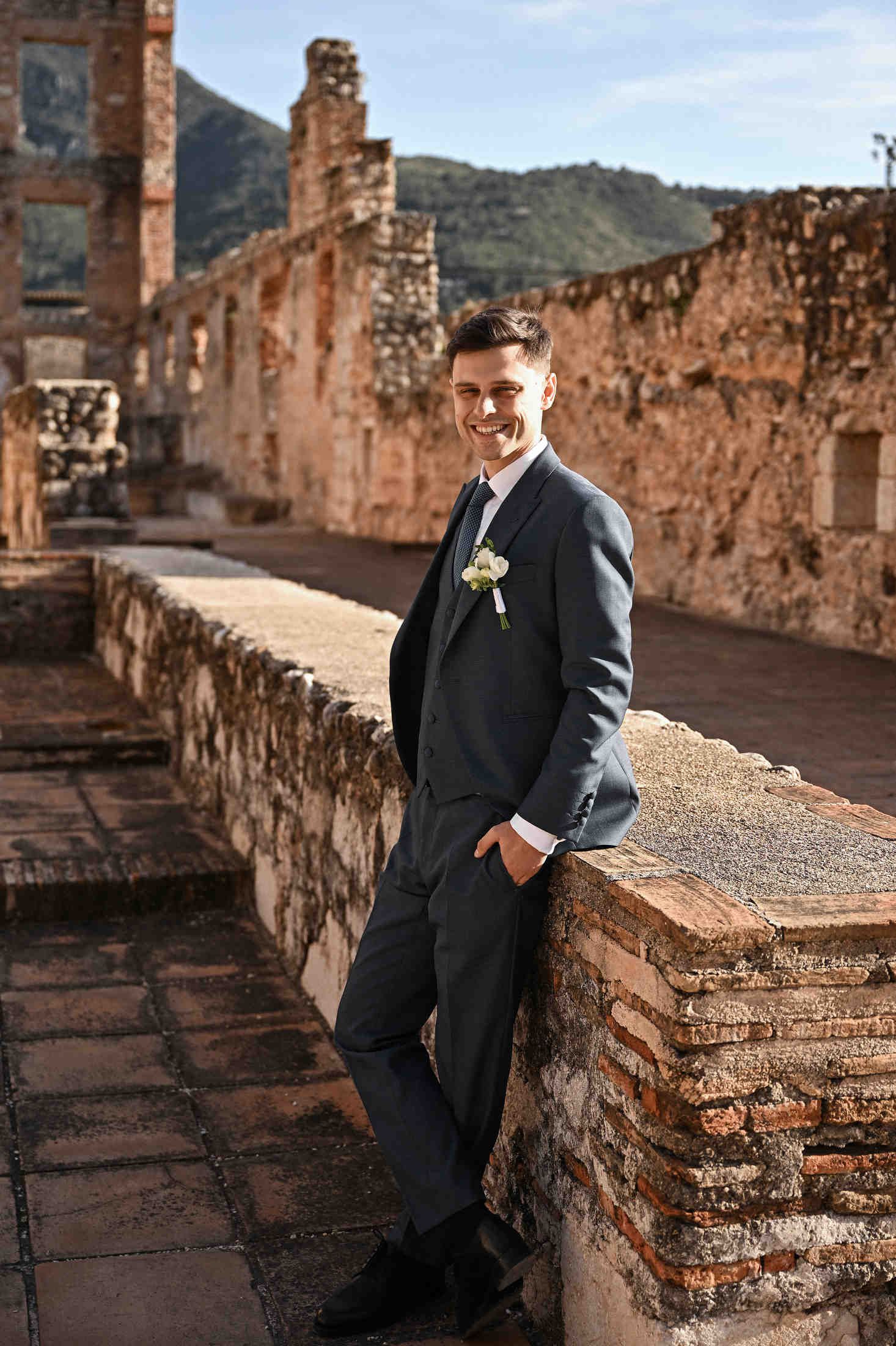 Smiling groom in a full-length shot among the ancient ruins and buildings of Monasterio de Santa María de la Valldigna in Valencia.