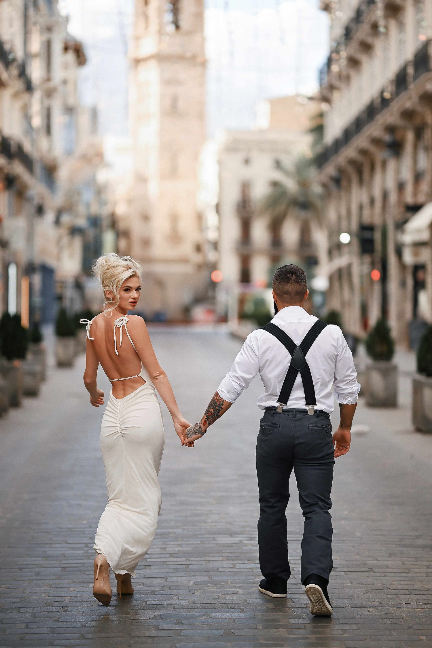 The bride and groom confidently walking in the pedestrian zone of Valencia. High-fashion street aesthetic and documentary vibe.