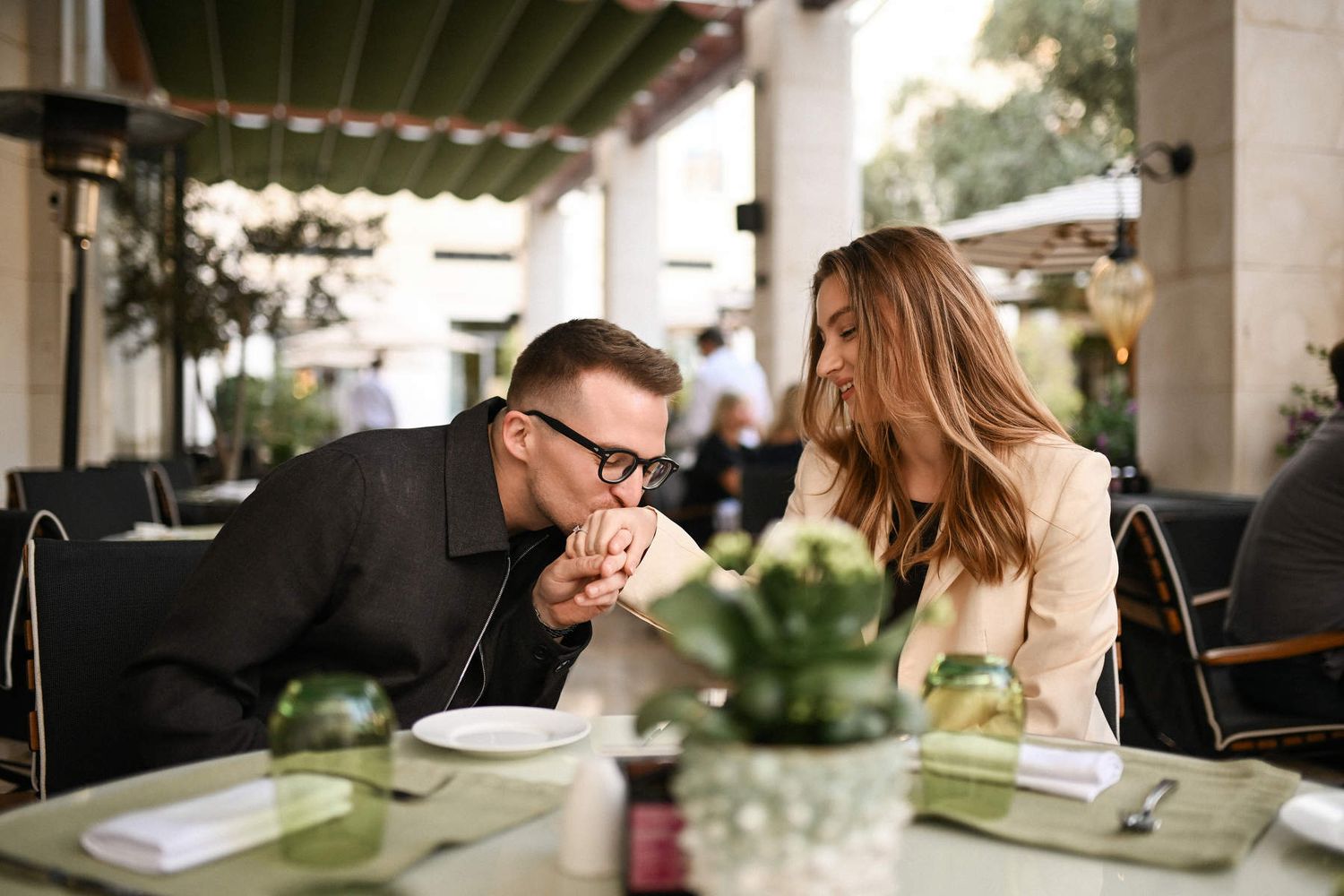 Romantic celebratory dinner in The Westin Valencia courtyard restaurant. A man lovingly kisses his fiancée's hand at the table.