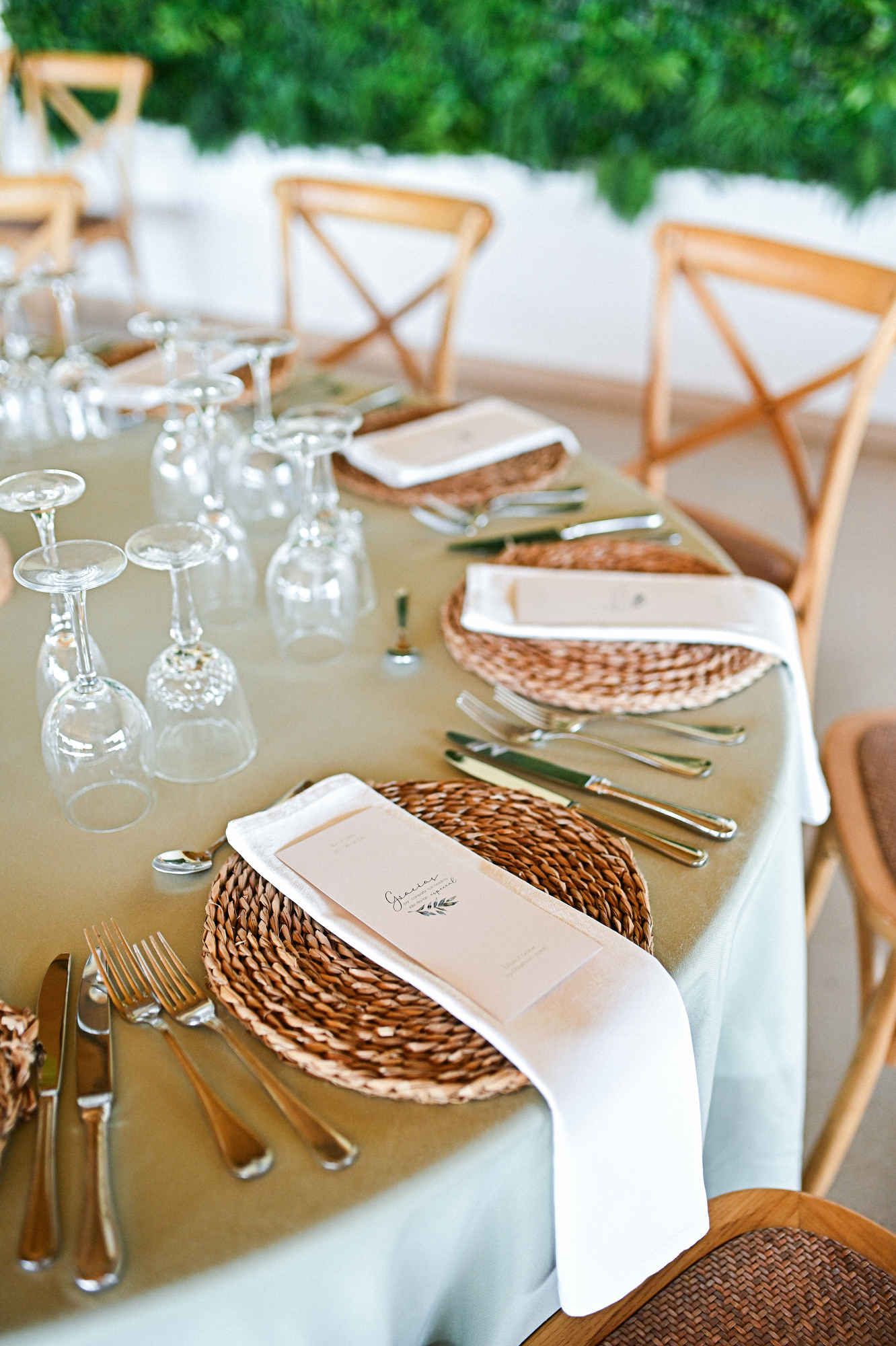 Elegant wedding table arrangement featuring woven placemats, folded napkins, and clear wine glasses.