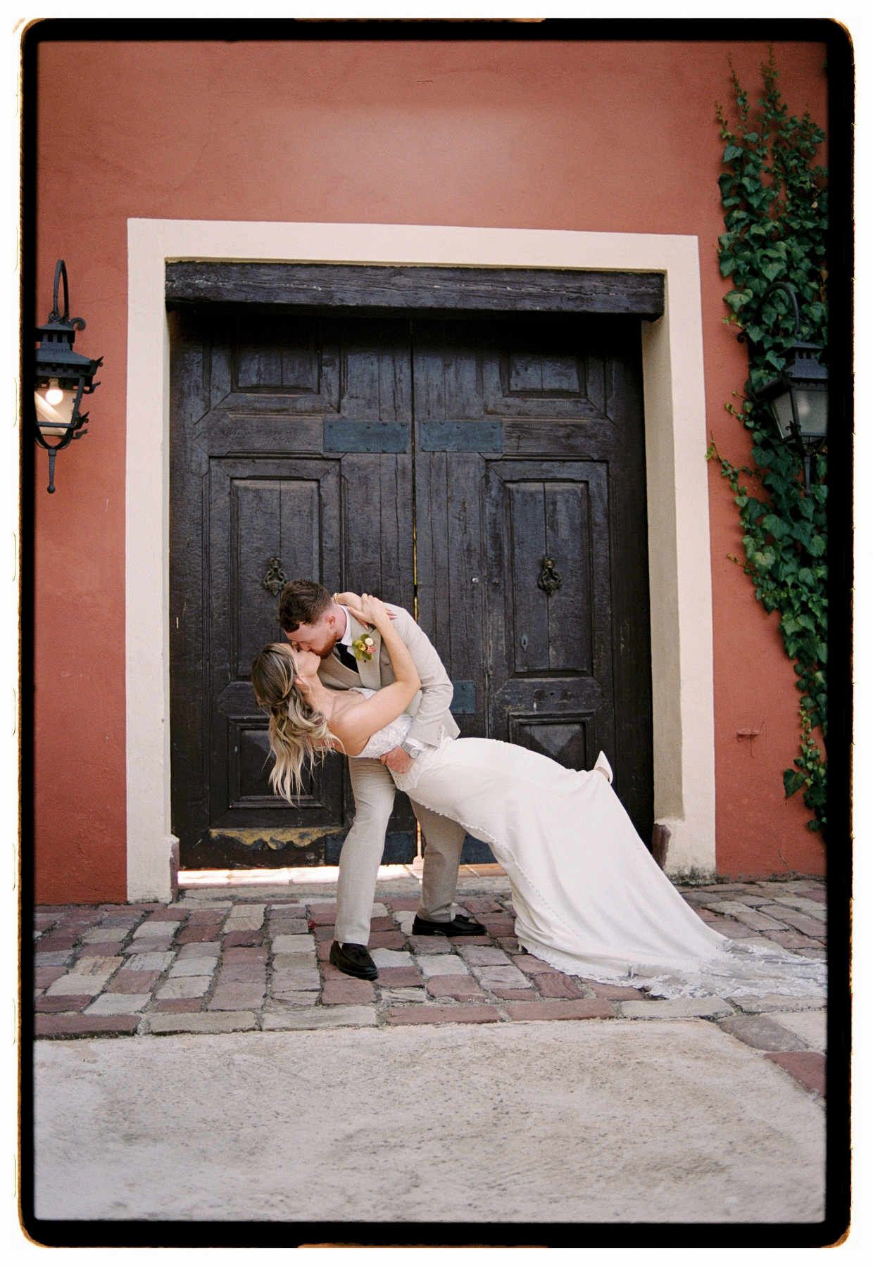 Groom dipping and kissing the bride in front of the historic gates at Villa Delia wedding venue.
