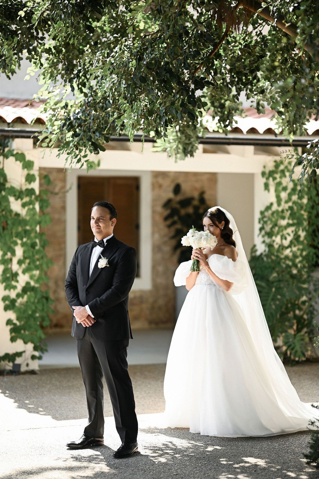 The bride playfully hiding behind her bouquet right before the first look reveal with the groom in the Finca del Canónigo courtyard.