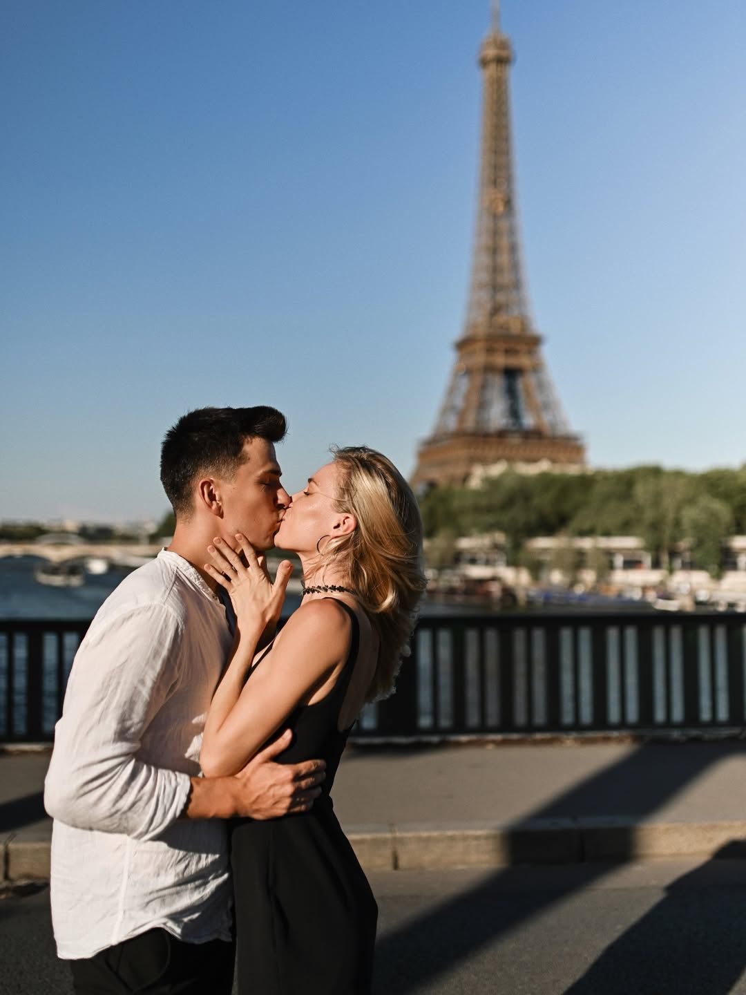 Engaged couple sharing a passionate kiss on Pont de Bir-Hakeim, showing off the new ring with the Eiffel Tower behind them.