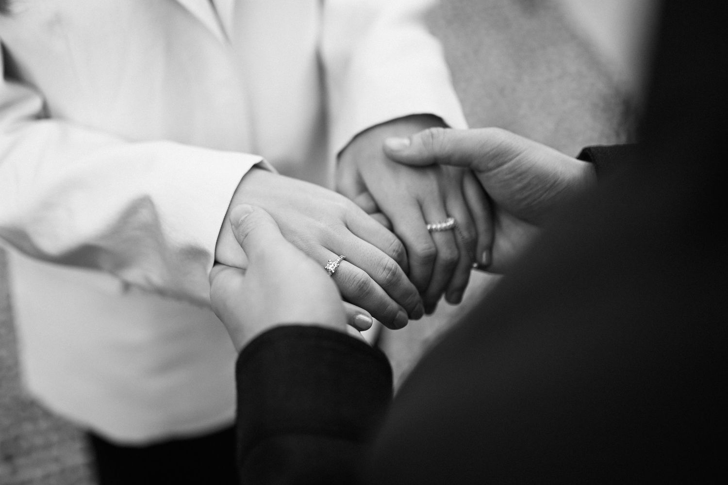 Black and white close-up of a newly engaged couple holding hands, highlighting the sparkling diamond ring.