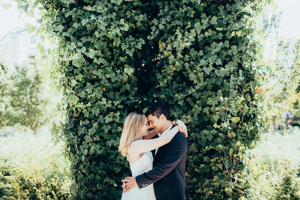 Romantic couple hugging intimately forehead to forehead against a dense wall of green ivy in a quiet Paris park setting.
