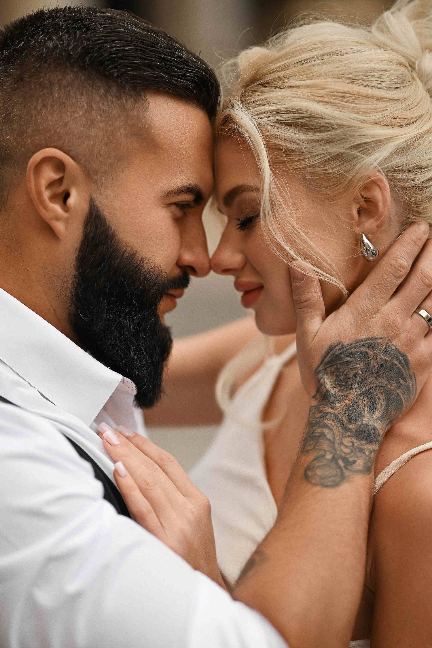 Editorial groom portrait. A close-up of a stylish groom with a beard and tattoos gently kissing the bride during a destination wedding