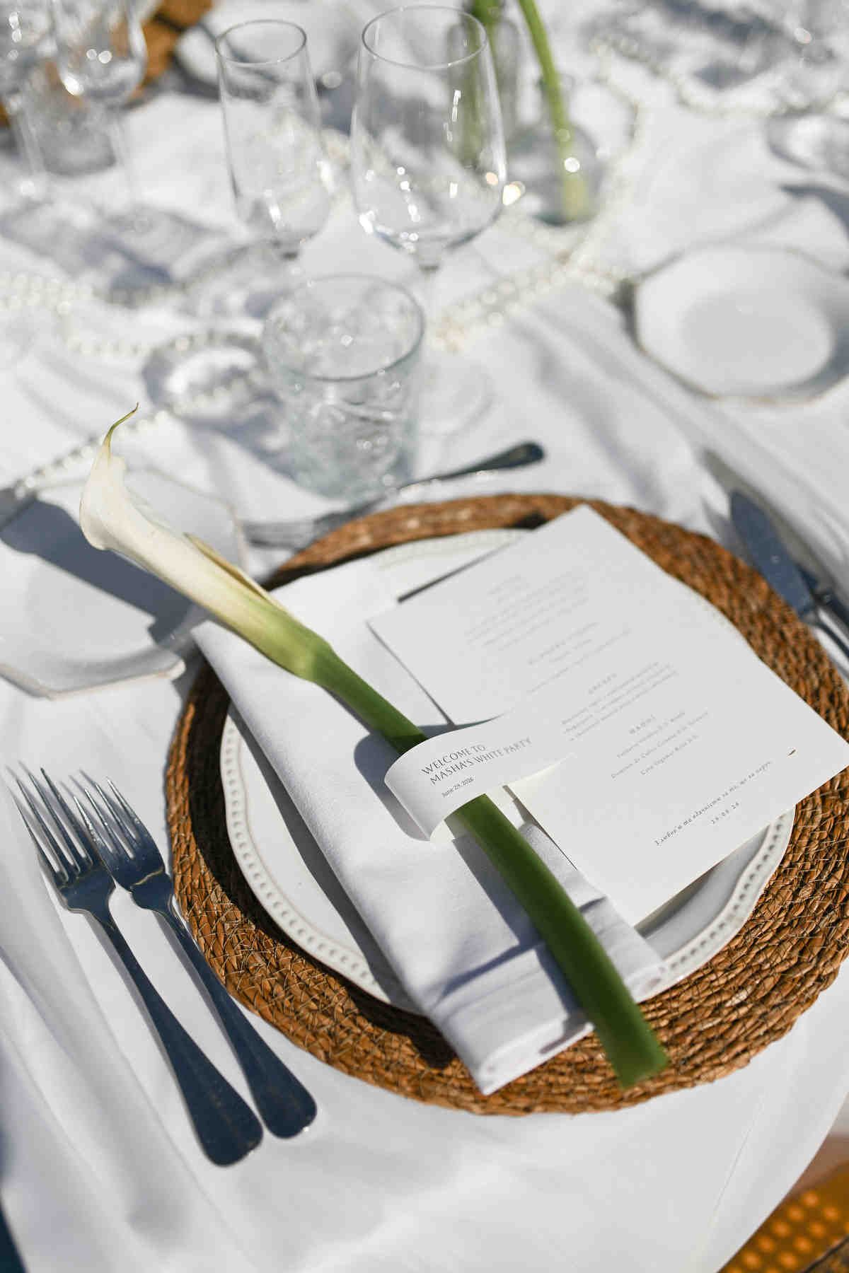 Elegant wedding table place setting at Alquería Kukala with a white calla lily, modern menu card, and woven placemat.
