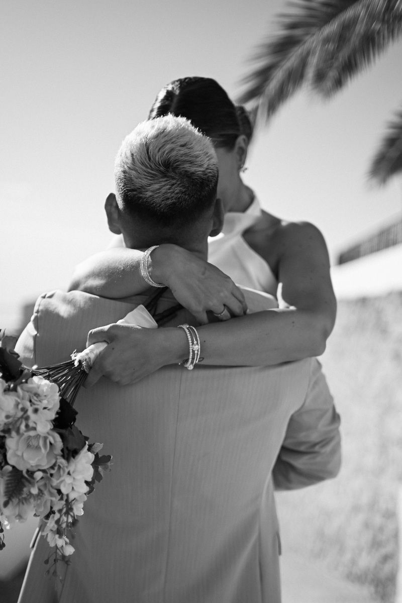 Black and white photo of a bride hugging the groom with her bouquet in hand on their wedding day.