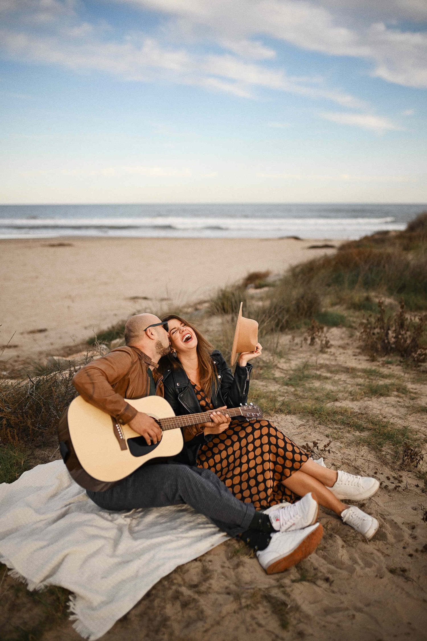 Engagement photographer in Valencia capturing a couple enjoying a beach picnic at El Saler while he plays a song