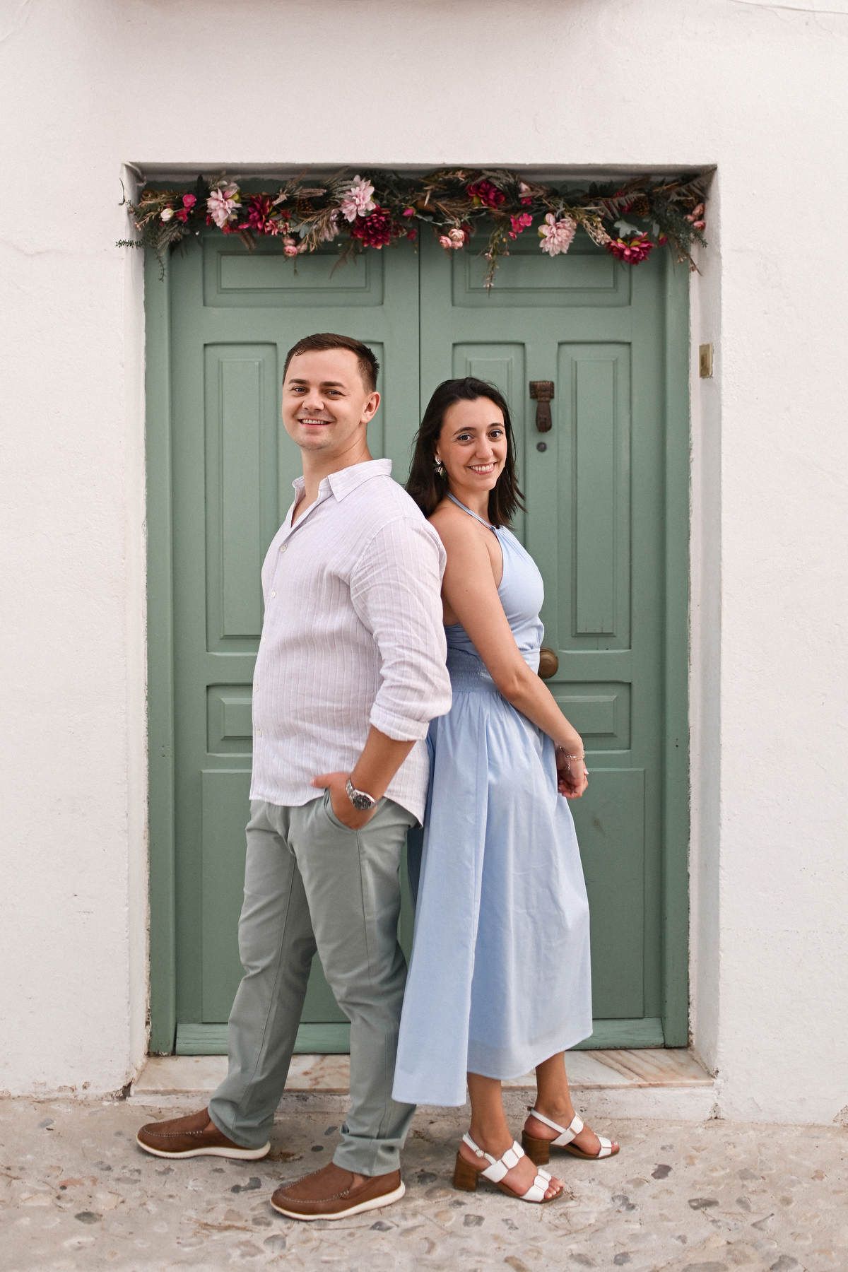 A couple stands back to back in front of a rustic green wooden door decorated with flowers after a surprise marriage in Altea.