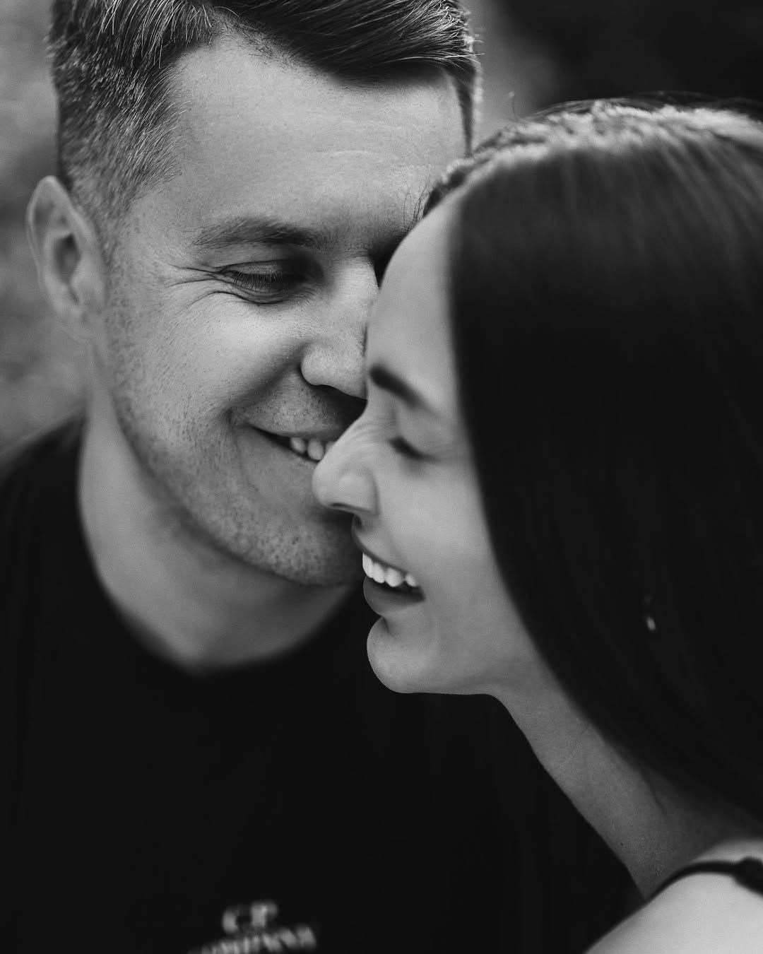 Black and white engagement portrait in Viveros Park featuring a man kissing his smiling fiancée on the cheek.