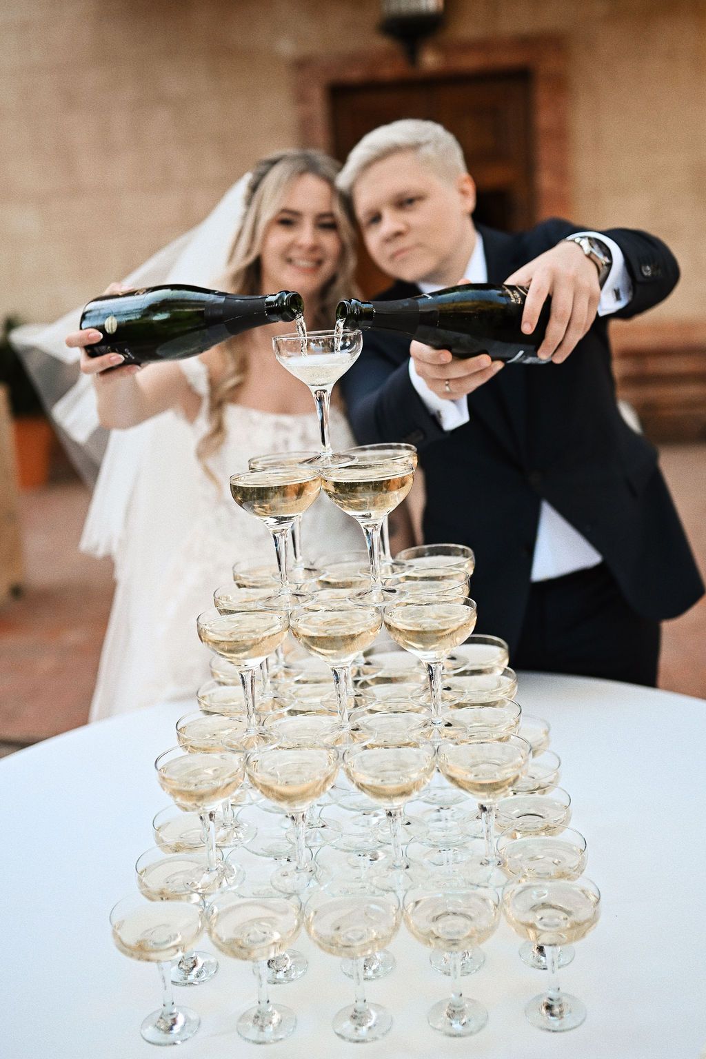 Newlyweds pouring champagne into a glass tower with the historic Benidorm villa backdrop at Finca El Senyoret wedding reception.