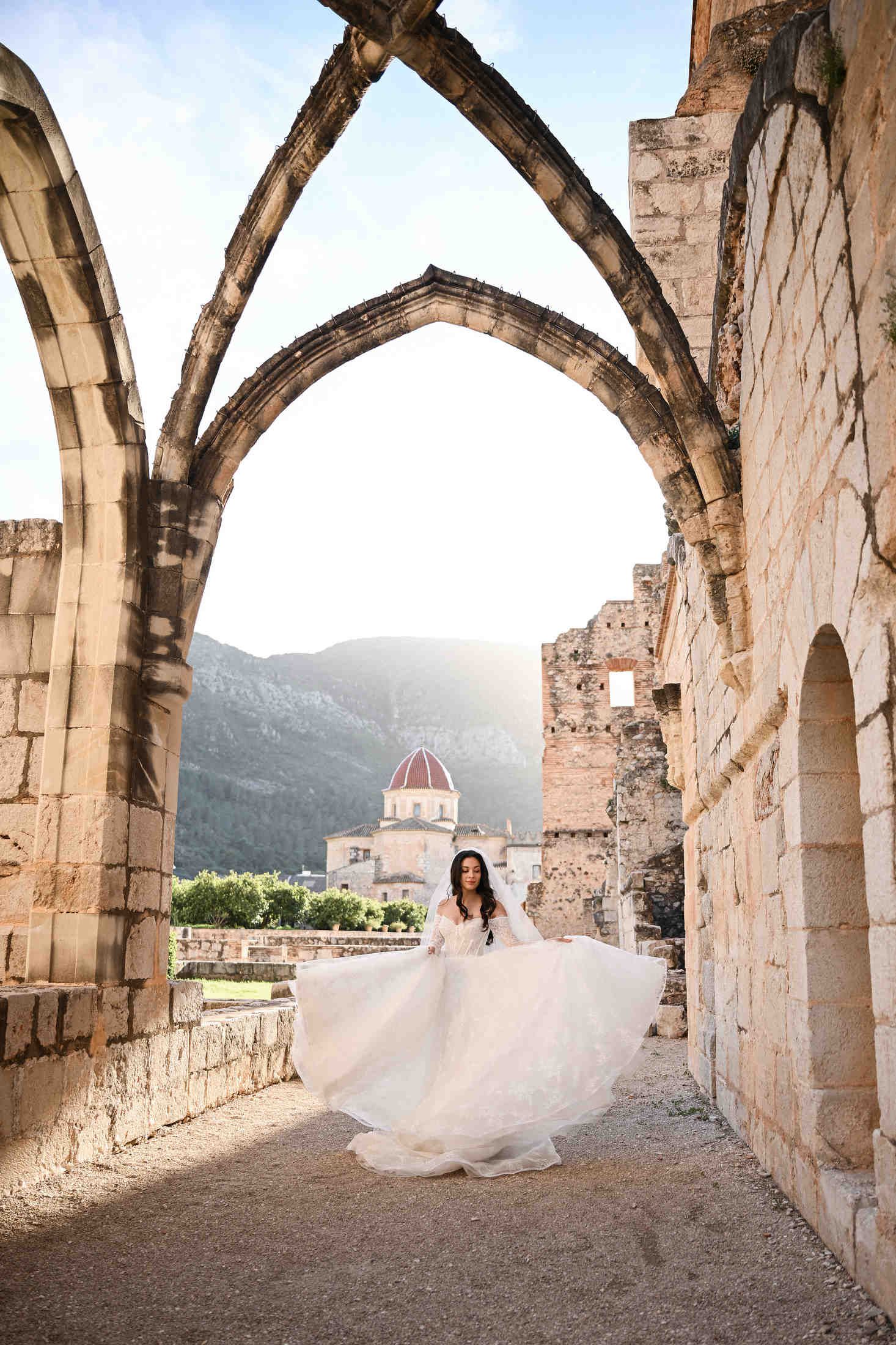 Bride twirling happily in her wedding dress among the ancient arches and historic buildings of Monasterio de Santa María de la Valldigna.