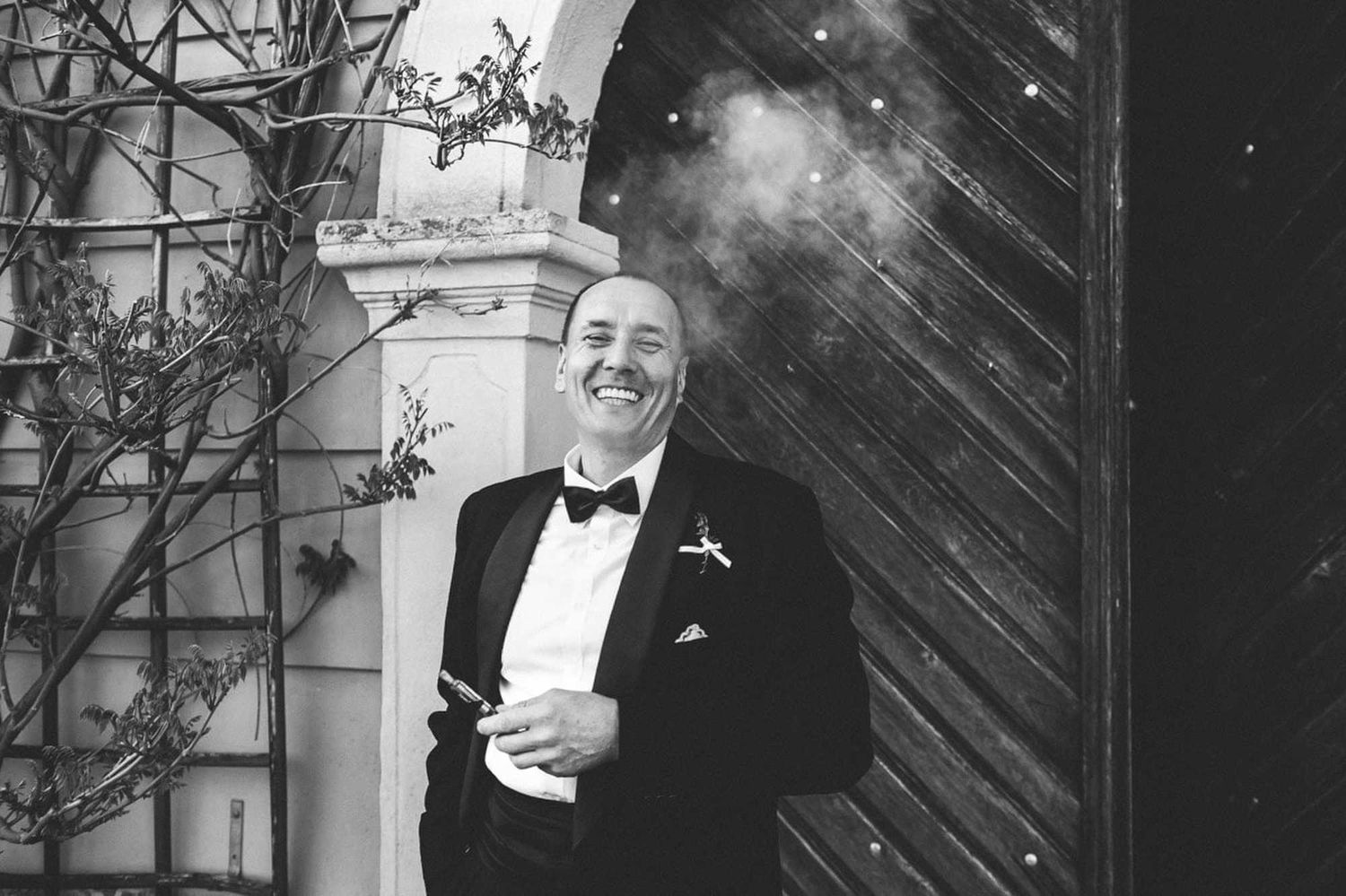 A wedding guest laughing and smoking a vape with an old European estate in the background. Authentic documentary wedding photography.