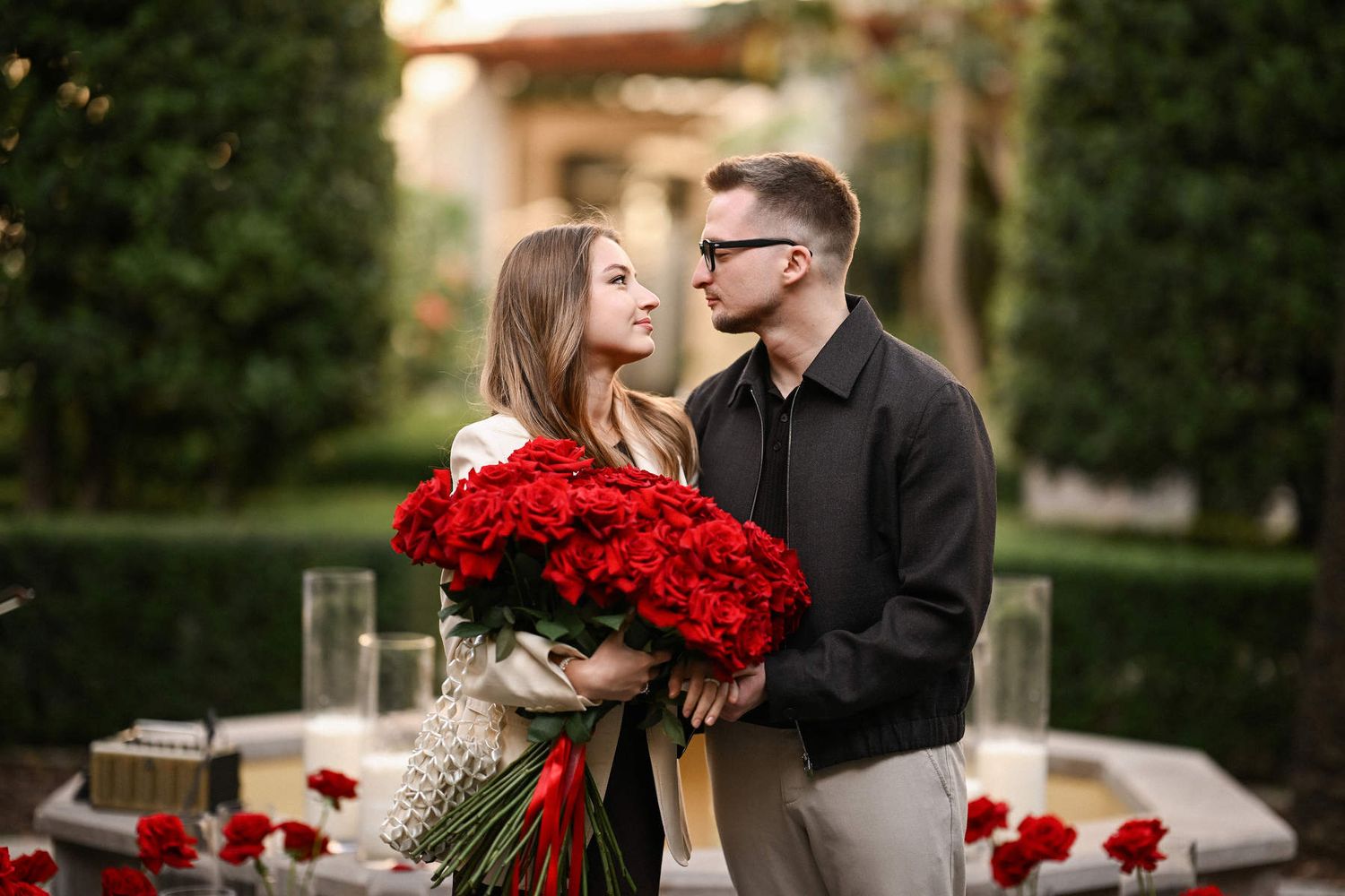 Newly engaged couple looking into each other's eyes while holding a bouquet of red roses in Valencia.