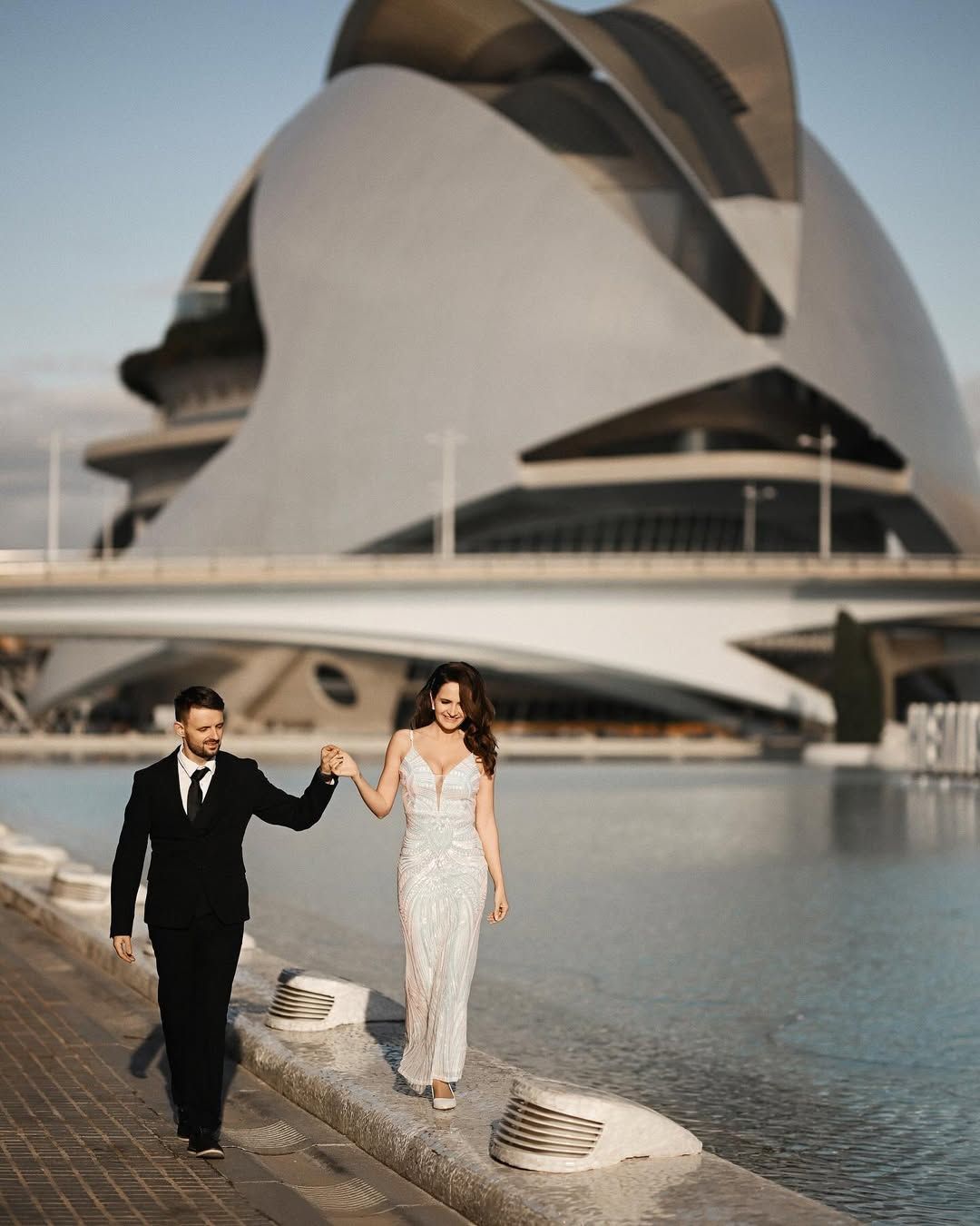 City of Arts and Sciences wedding photography in Valencia, showing a bride and groom holding hands walking near blue water.
