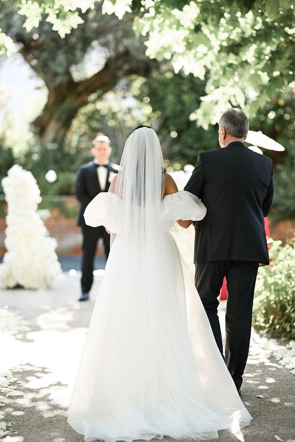 Back view of the father walking the bride down the aisle, showcasing the stunning long train of her wedding dress at Finca del Canónigo.