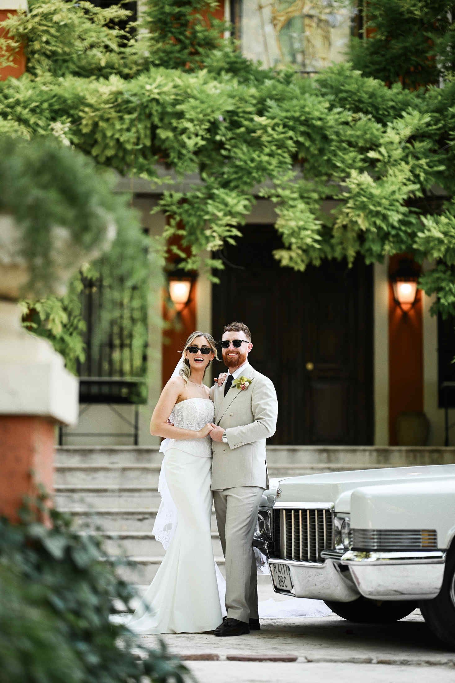 Happy newlyweds smiling and posing for a photographer against the historic luxury facade of Villa Dela in Valencia.