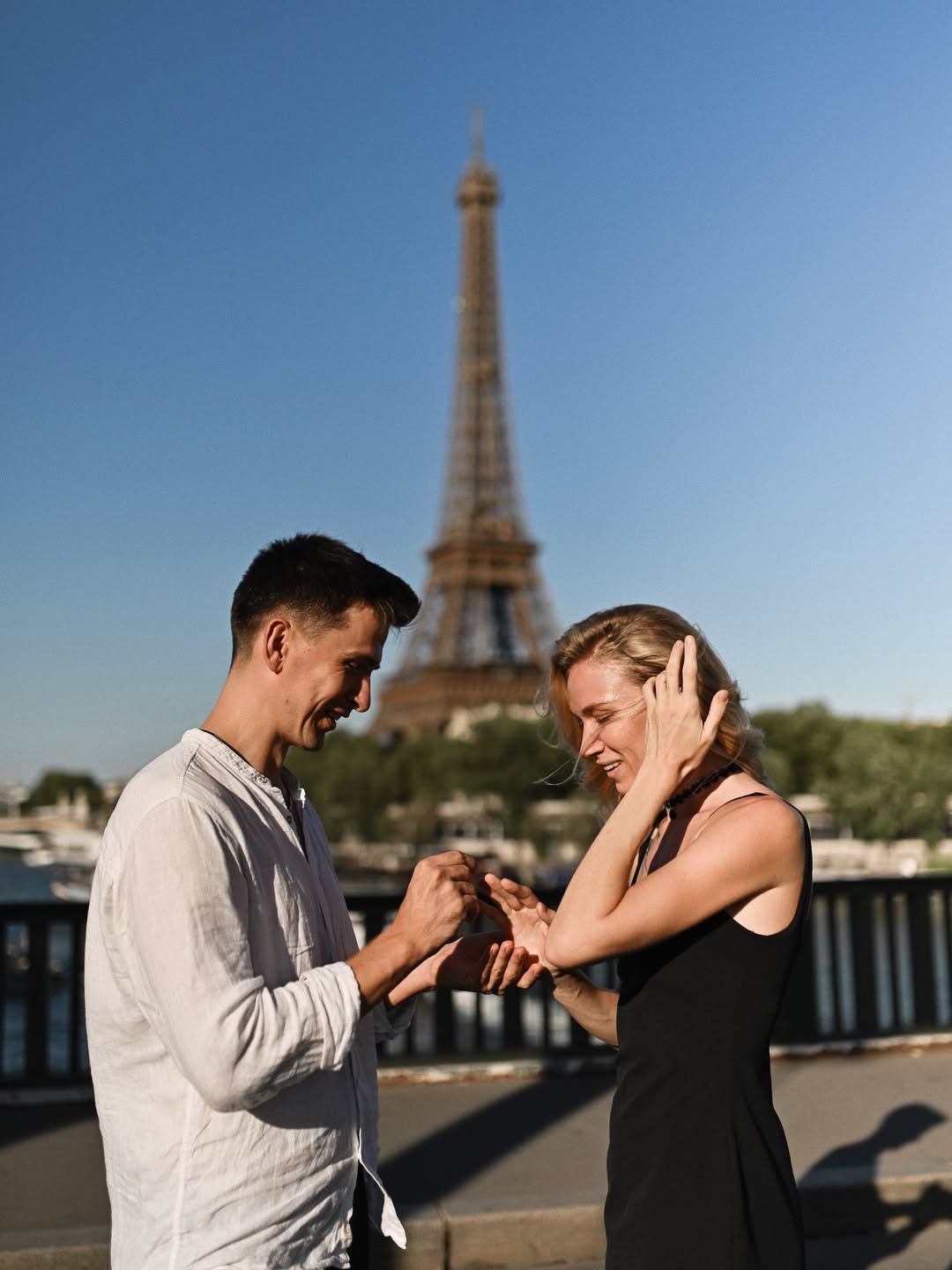 Man standing and offering a ring to a surprised woman during a Paris proposal with the Eiffel Tower in clear evening sunlight.