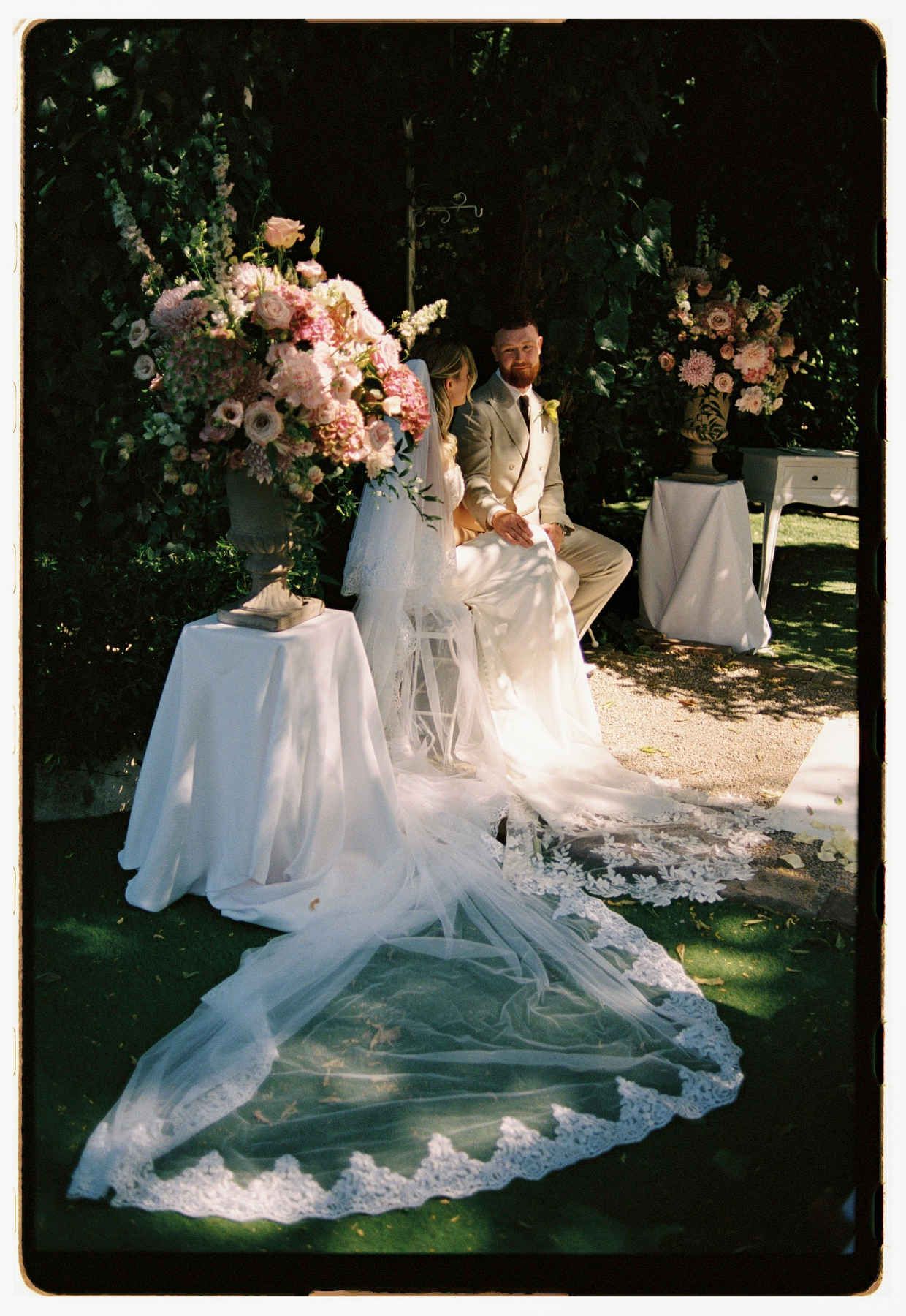 Happy bride and groom sitting during their wedding ceremony, highlighting the bride's beautiful long veil.