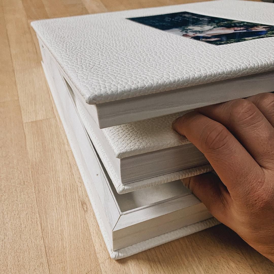 Photographer packing white leather wedding albums with professional designer layouts into a premium gift box.