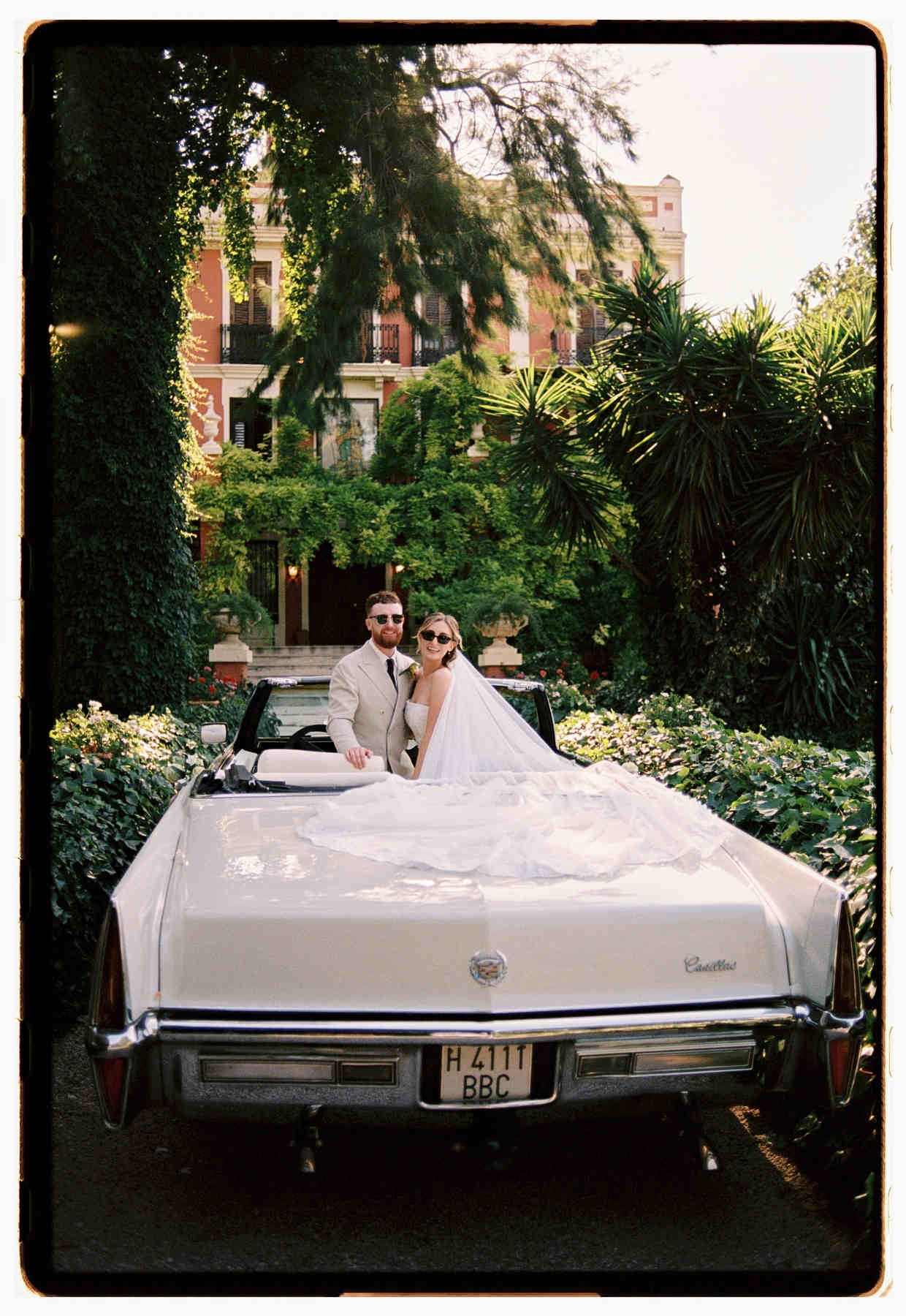 Wide cinematic shot of the bride and groom in a vintage Cadillac with the beautiful Villa Delia facade.