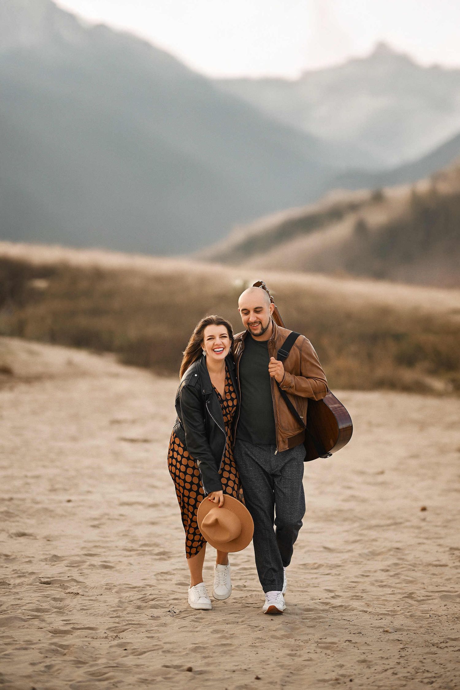 Smiling couple looking at the camera while walking along the sandy Valencia coast for their pre-wedding photoshoot