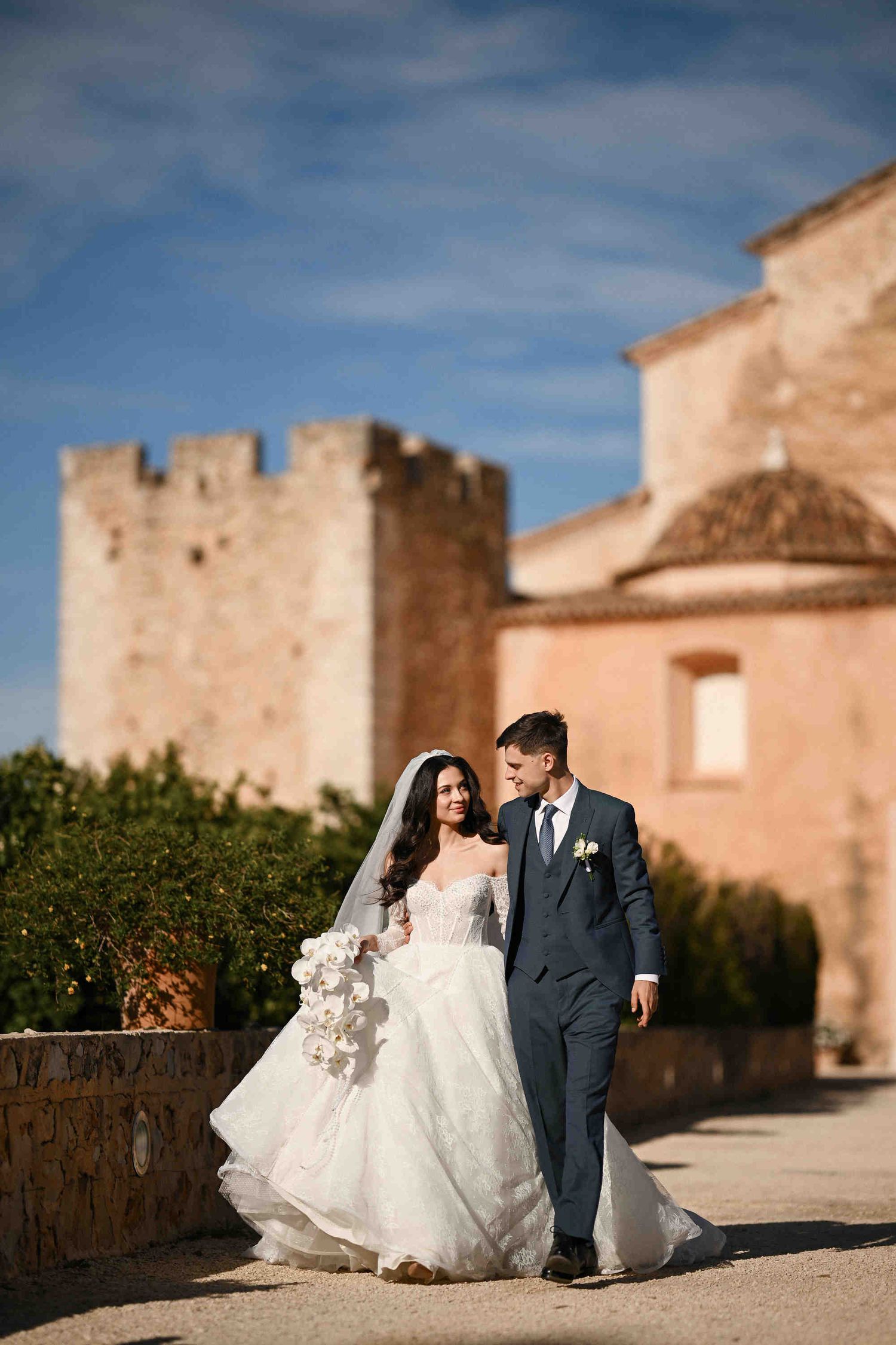Newlyweds strolling through the ancient monastery courtyard, highlighting the elegant bridal gown against weathered stone walls in Valencia.