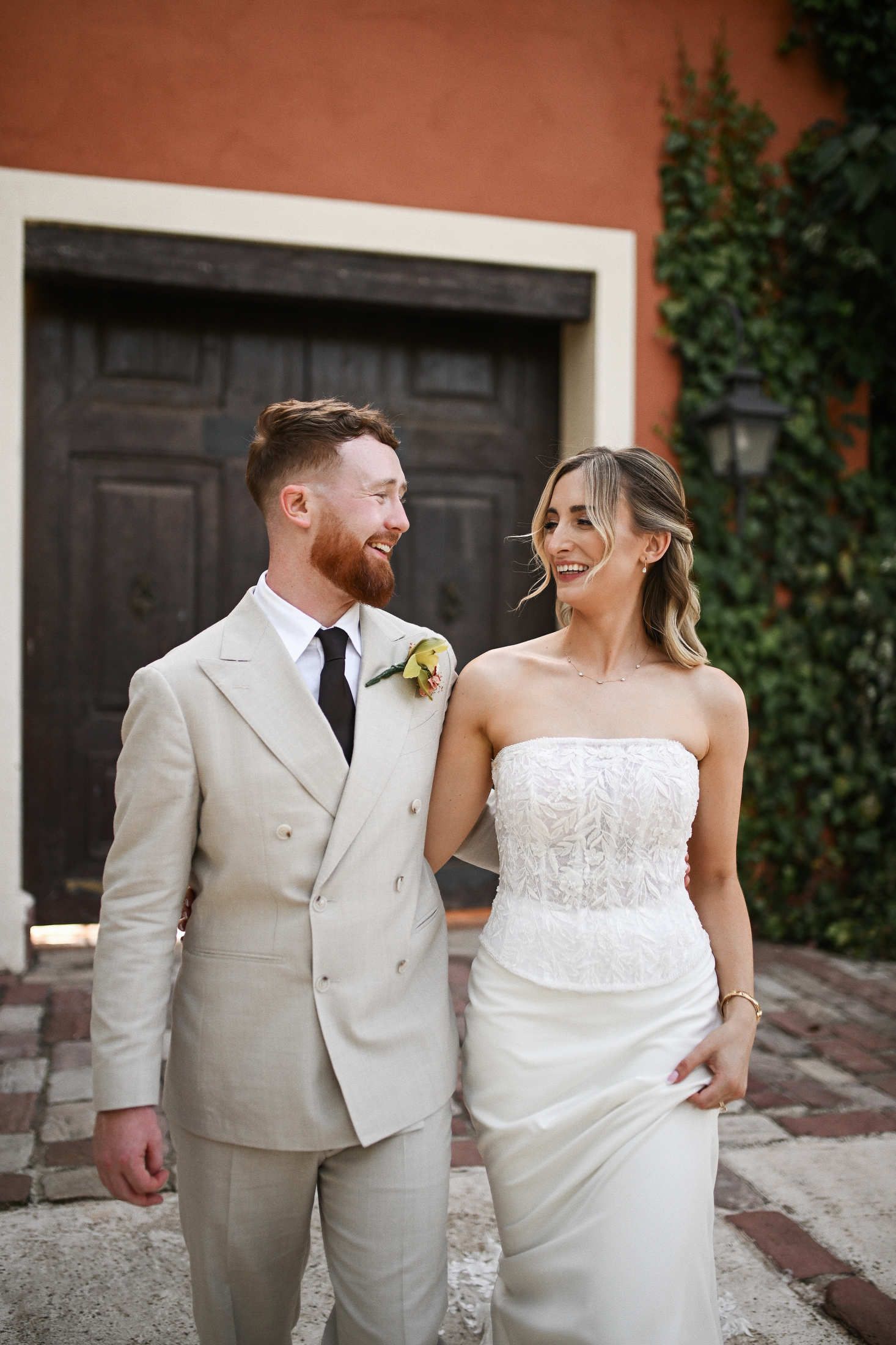 Bride and groom walking together near the vintage gates and historic facade of Villa Dela wedding venue in Valencia.