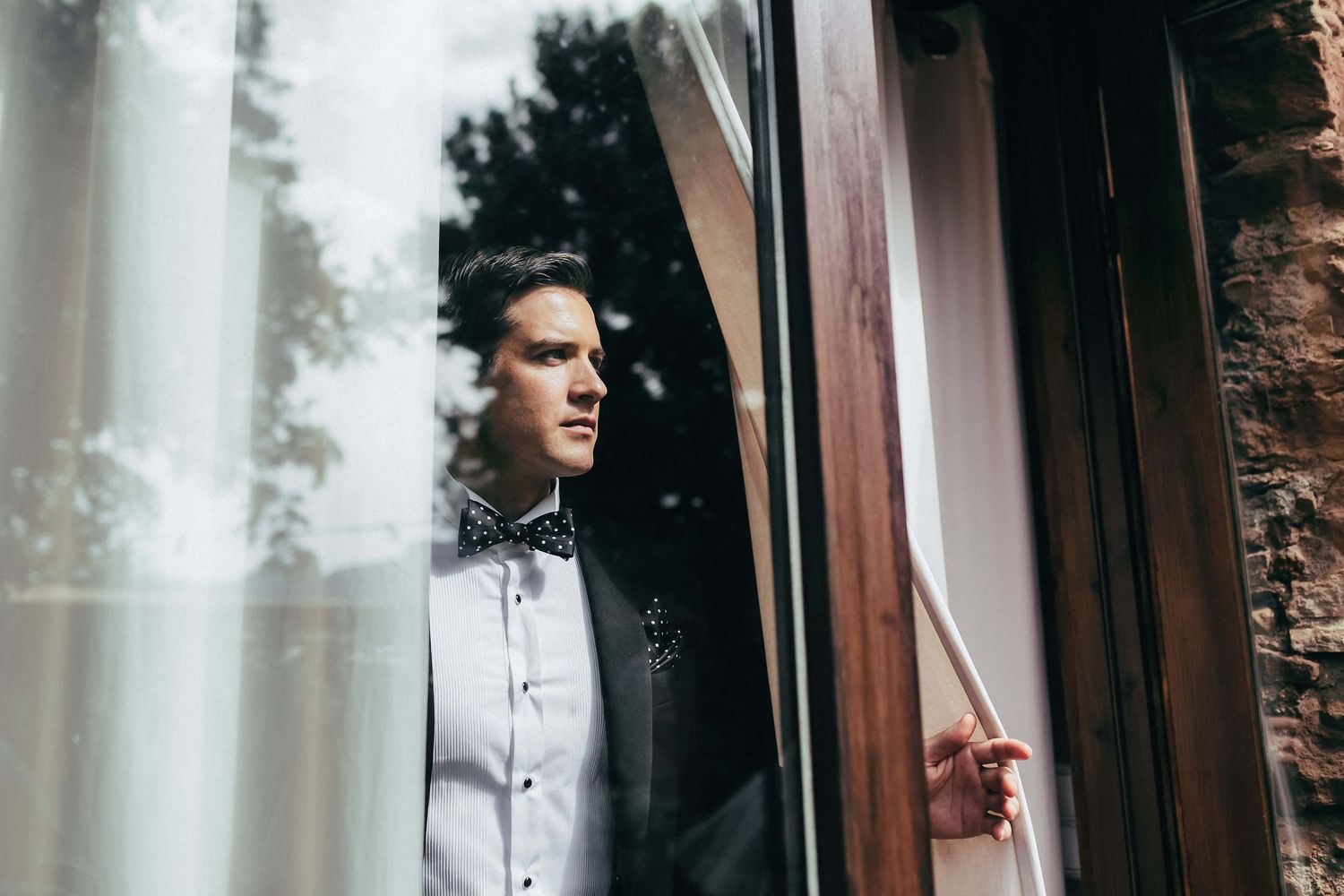 The groom ready for the ceremony, watching guests arrive from the villa. A quiet moment of anticipation at Masia El Follo, Catalonia