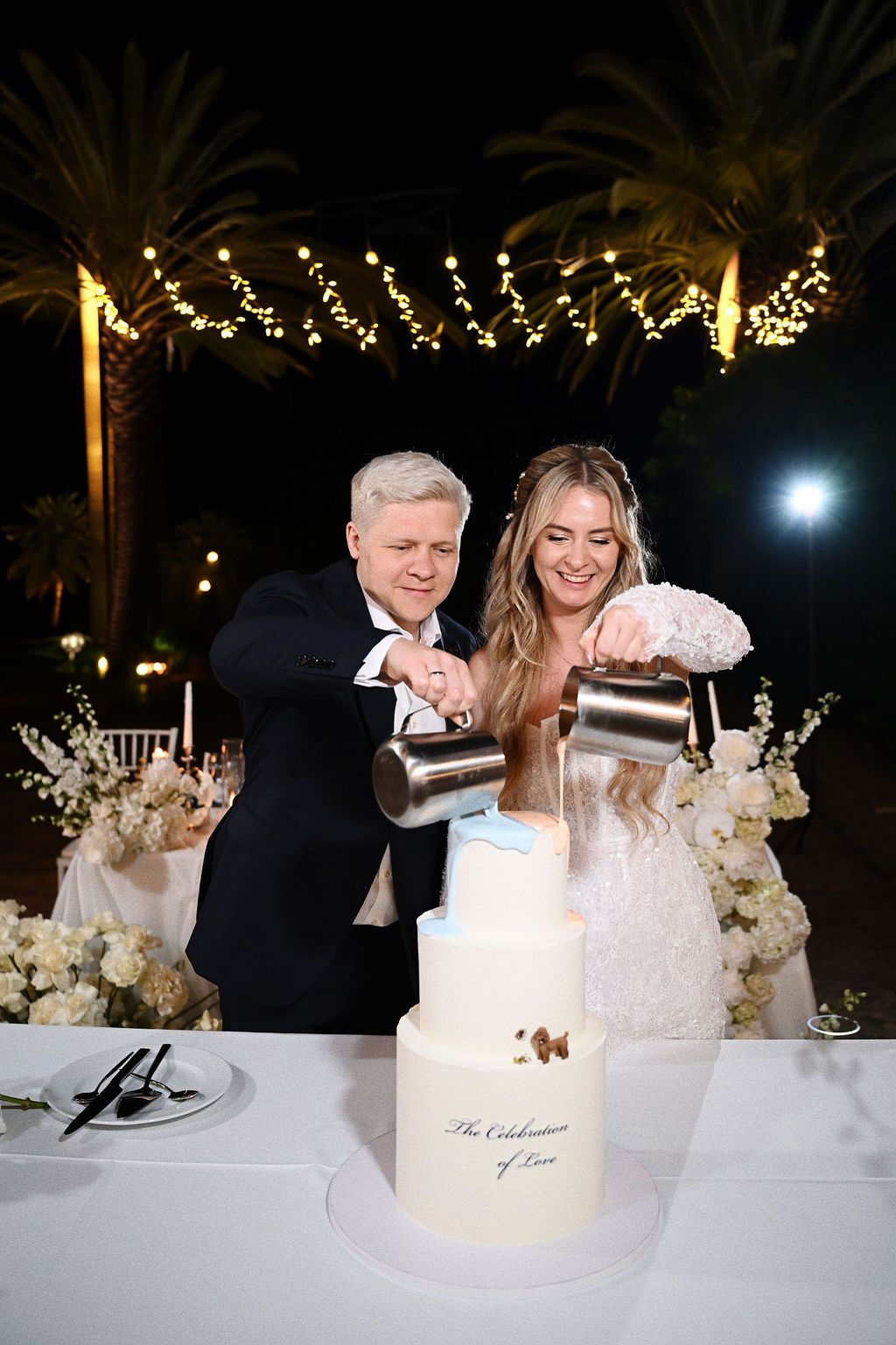 The wedding couple pouring glaze over their wedding cake during the open-air reception at Finca El Senyoret in the Benidorm area.