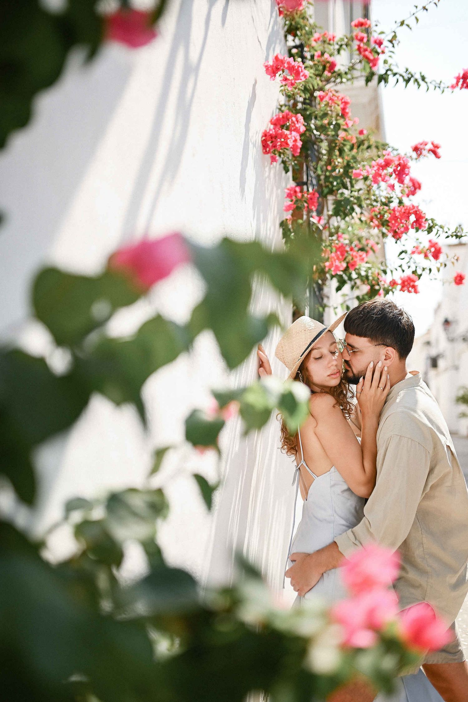 A romantic couple embracing amidst blooming pink flowers in the picturesque streets of Altea's old town