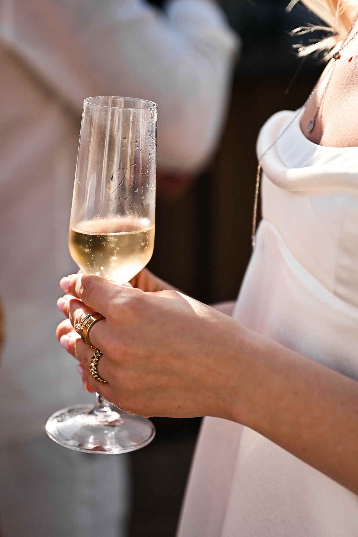 Close-up of a bride in a white dress holding a glass of champagne, showing elegant gold wedding rings.