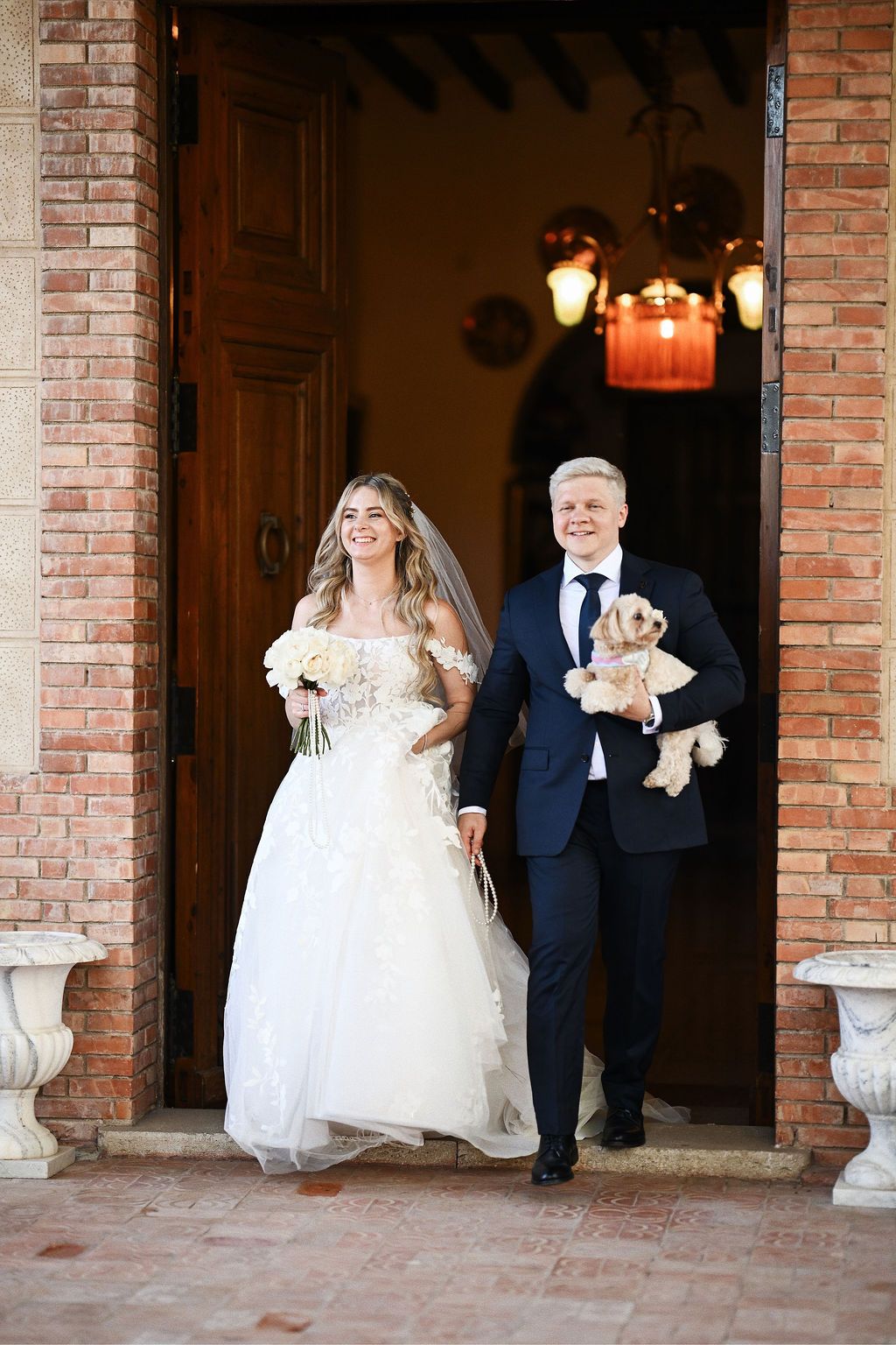 Bride and groom carrying their dog while walking out to cheering guests at Finca El Senyoret. Emotional Benidorm wedding photography.
